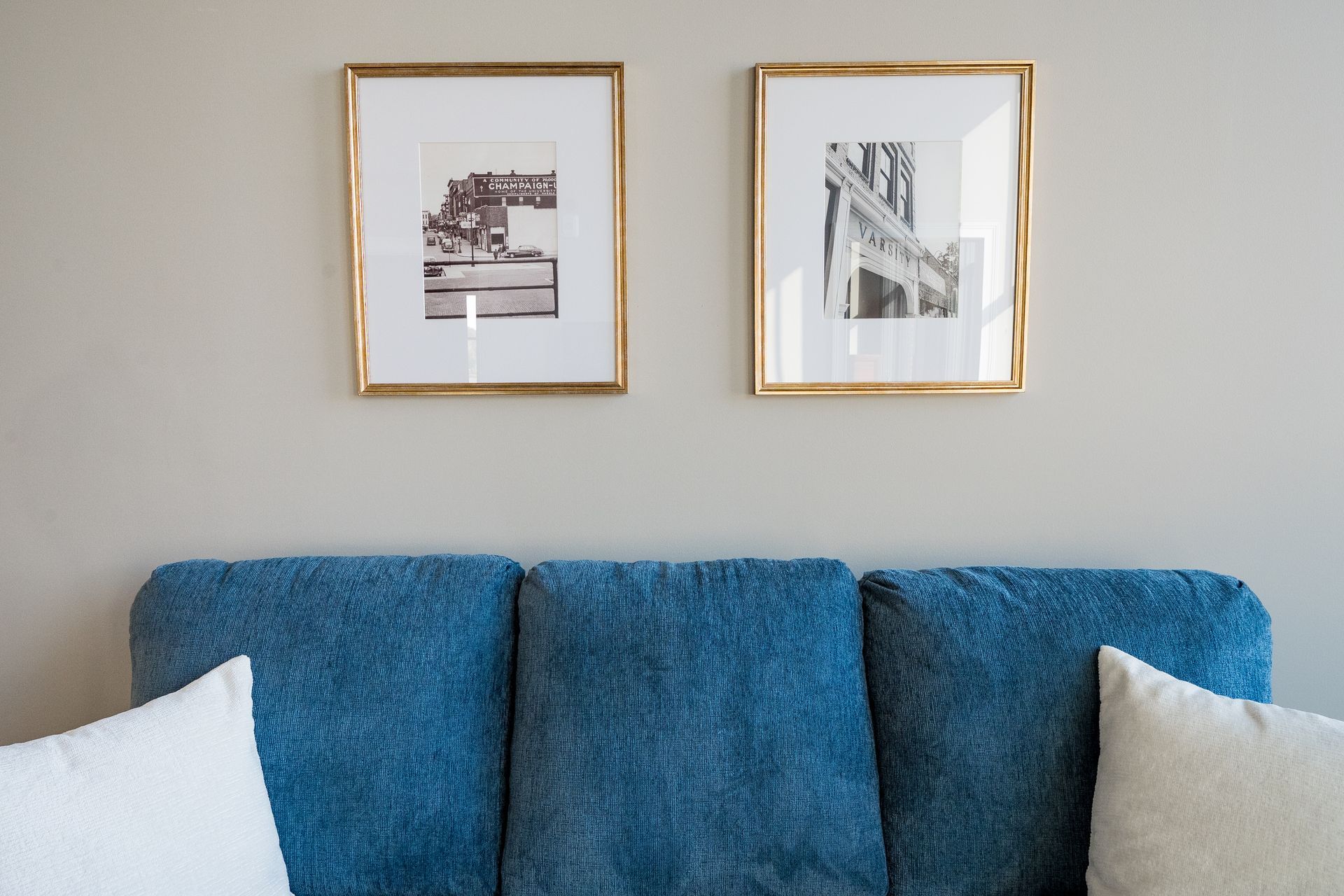 Blue sofa beneath two framed prints on a beige wall with white pillows on either side