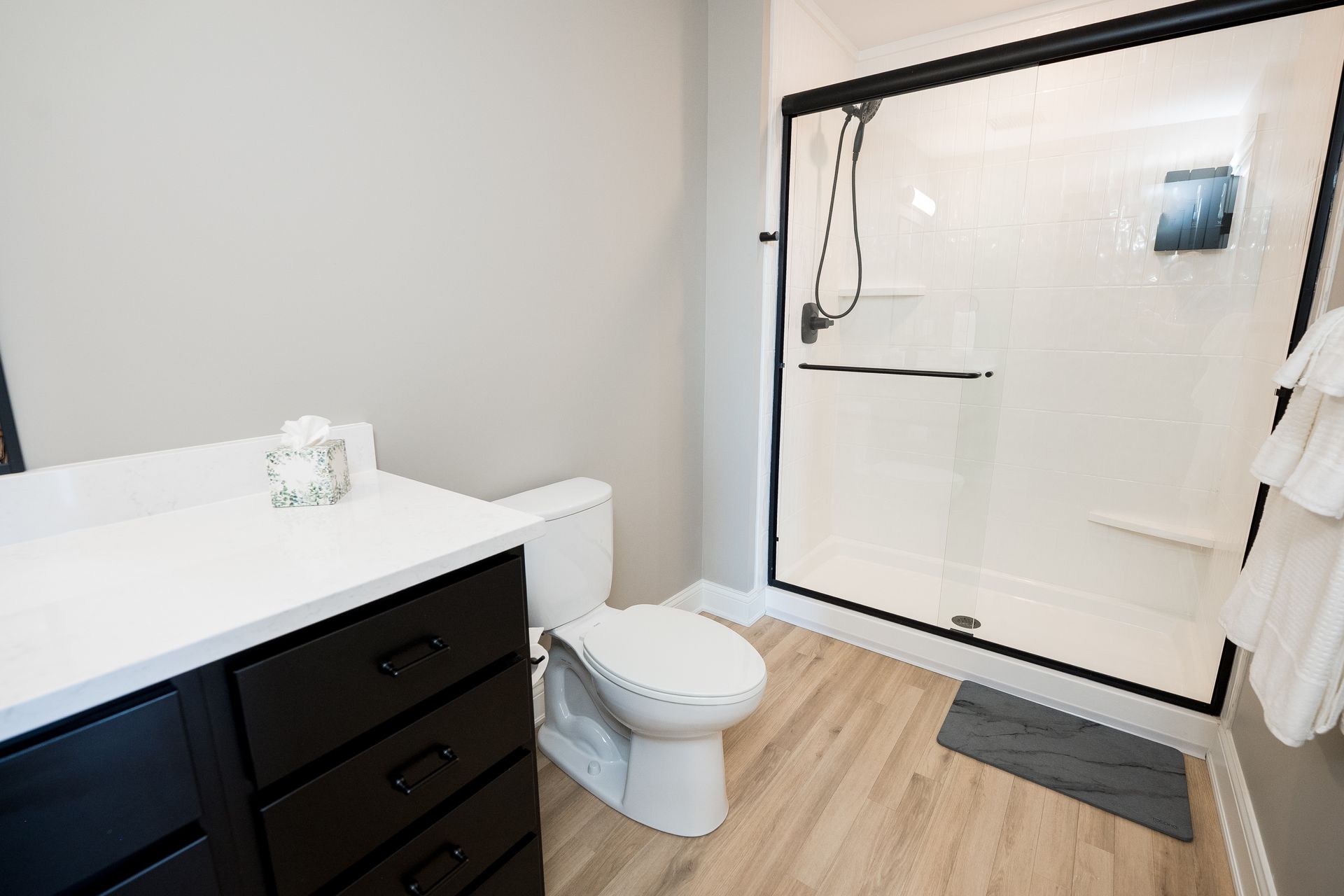Modern bathroom with white vanity, toilet, and glass shower door on wood-look flooring