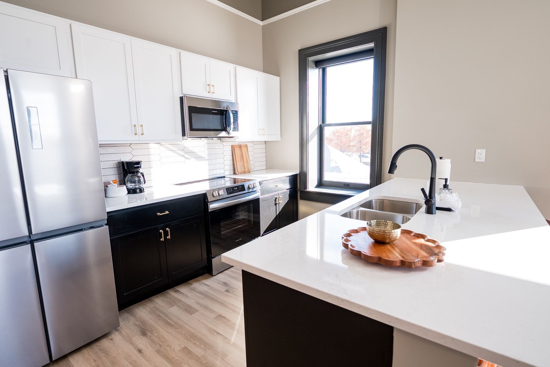 Modern kitchen with white cabinets, stainless steel appliances, black stove, and white island with fruit bowl.
