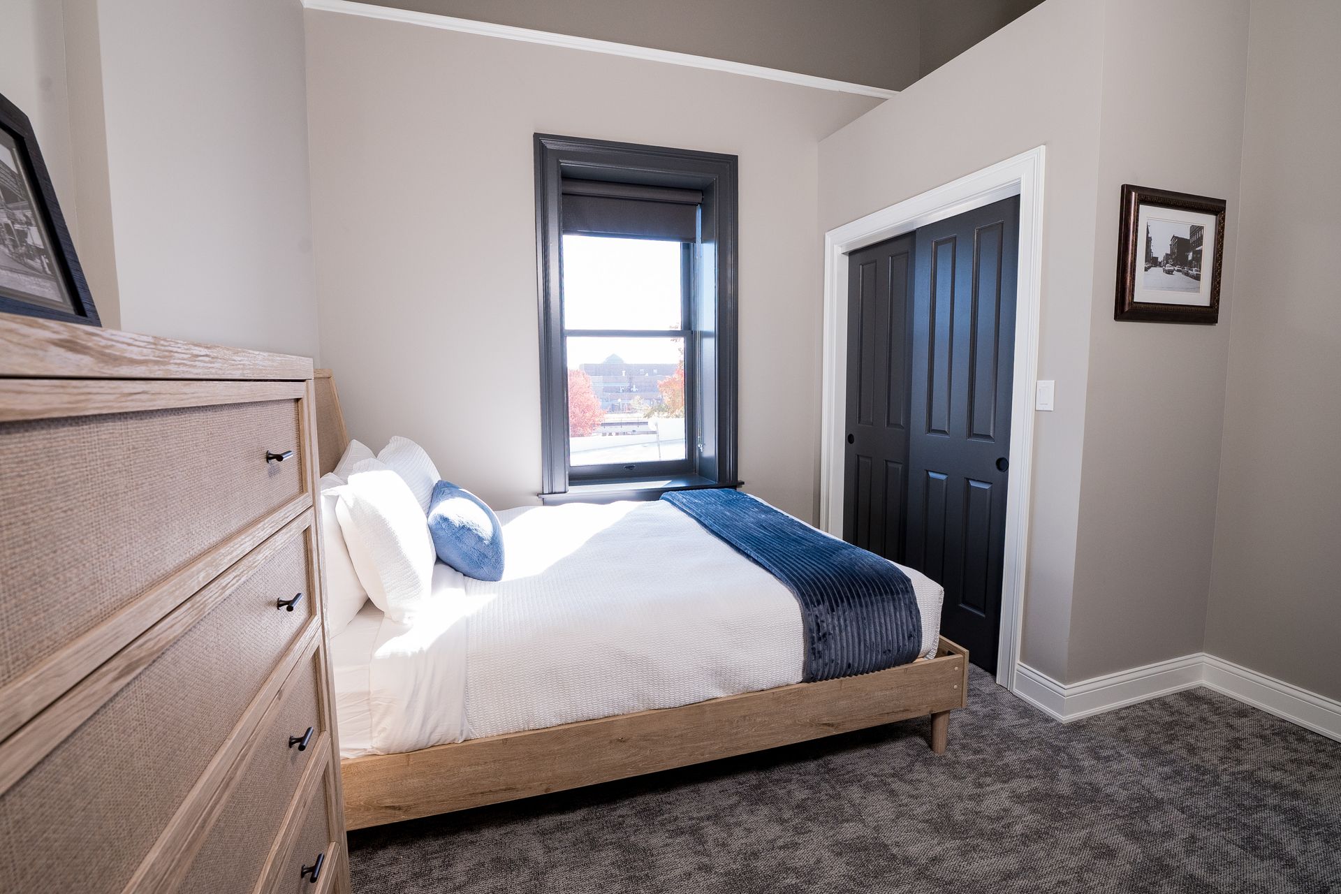 Bright bedroom with white bed, blue bedding, gray walls, carpet, window, and closet doors