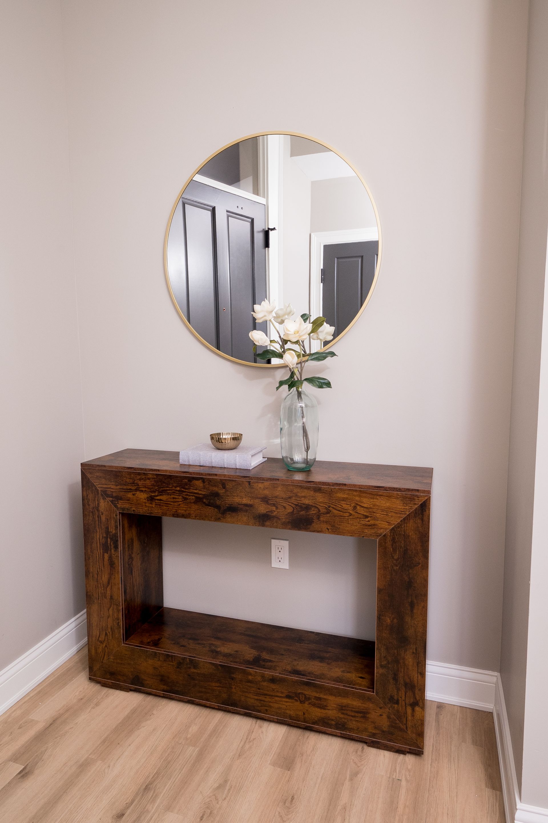 Rustic wooden console table with a round mirror and white flowers in a minimalist hallway