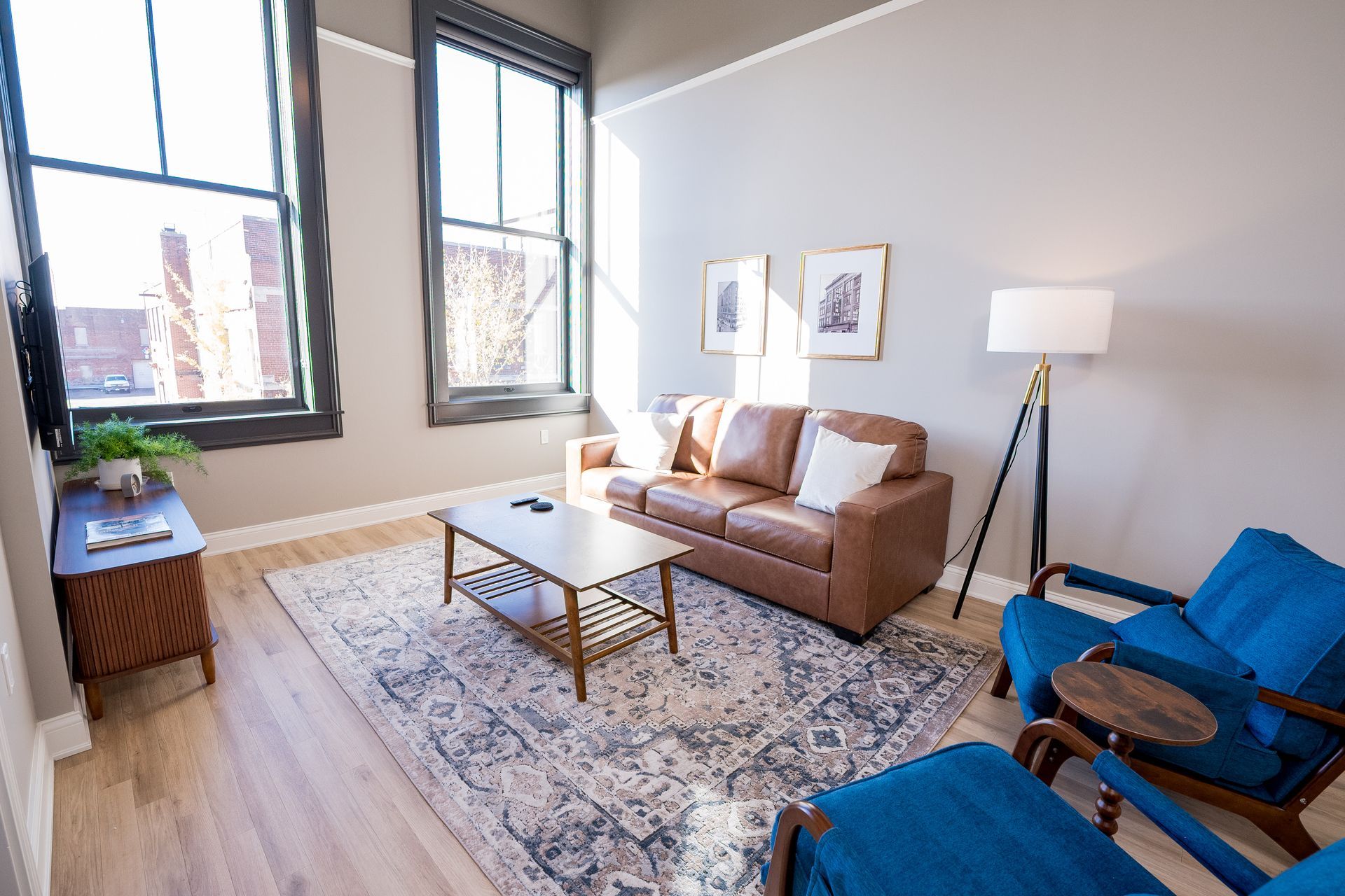 Bright living room with a tan sofa, blue chair, coffee table, lamp, rug, and large windows