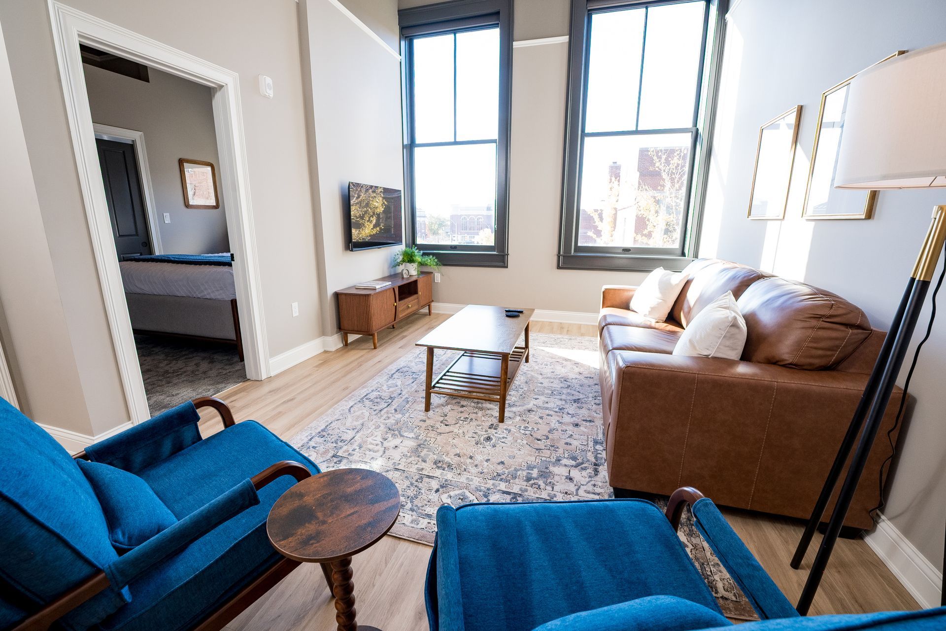 Bright living room with blue chairs, tan sofa, coffee table, and large windows letting in sunlight