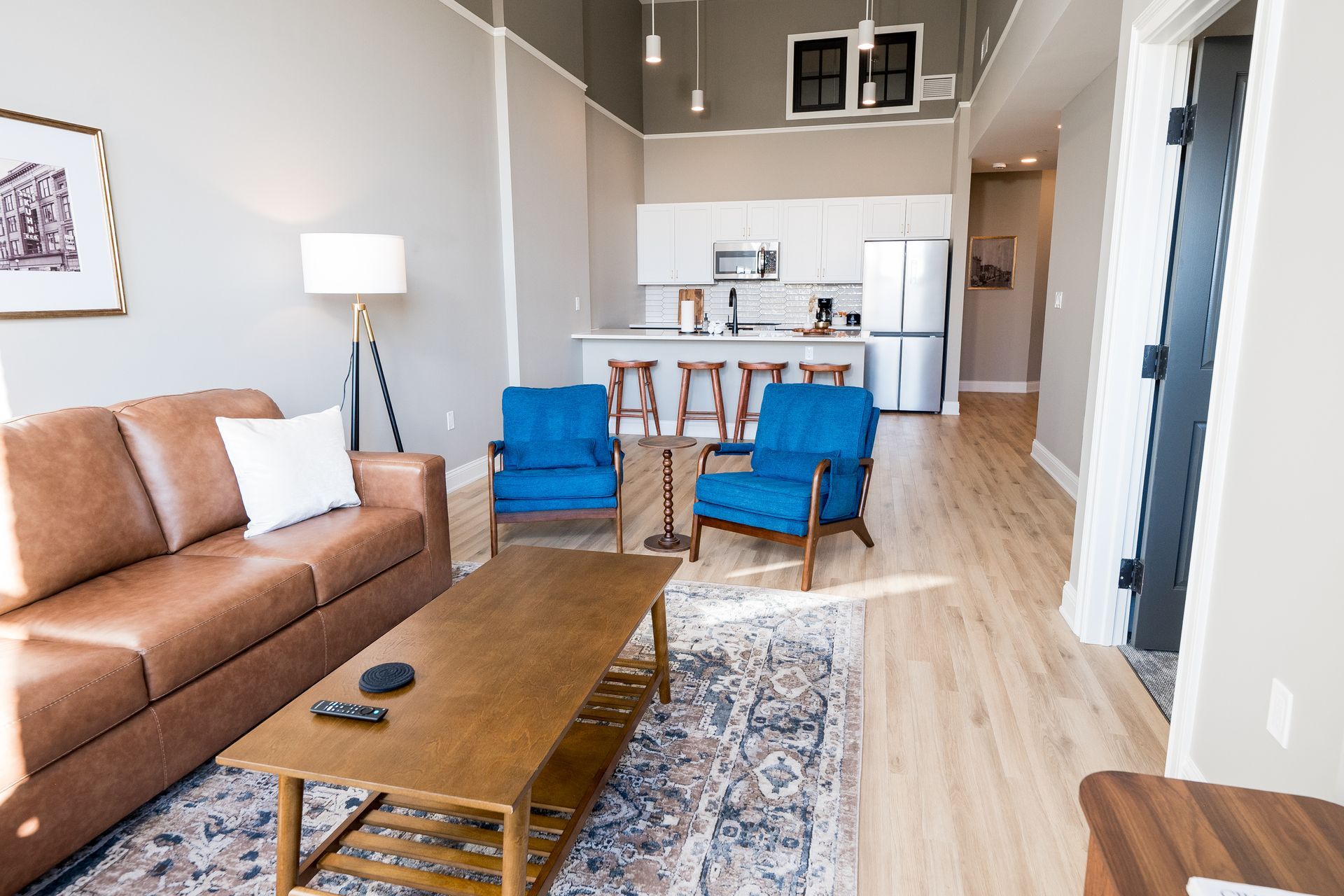 Modern living room with brown sofa, blue chairs, coffee table, and open kitchen in the background