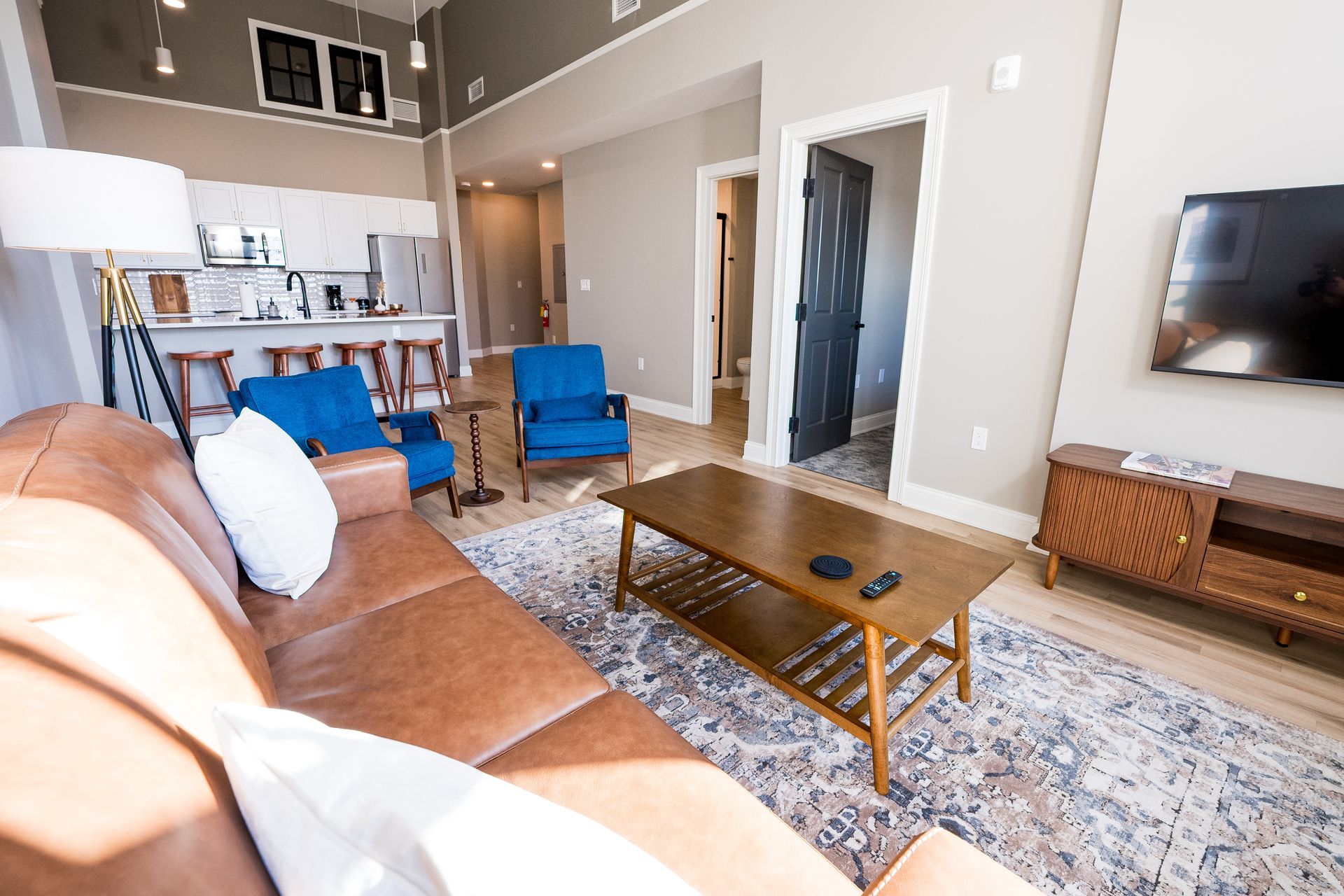Bright living room with tan sofa, blue chairs, coffee table, rug, and wall-mounted TV