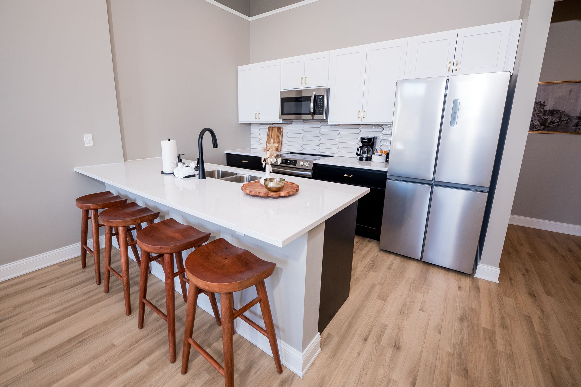Modern kitchen with white island, four wooden stools, stainless appliances, and light wood floors