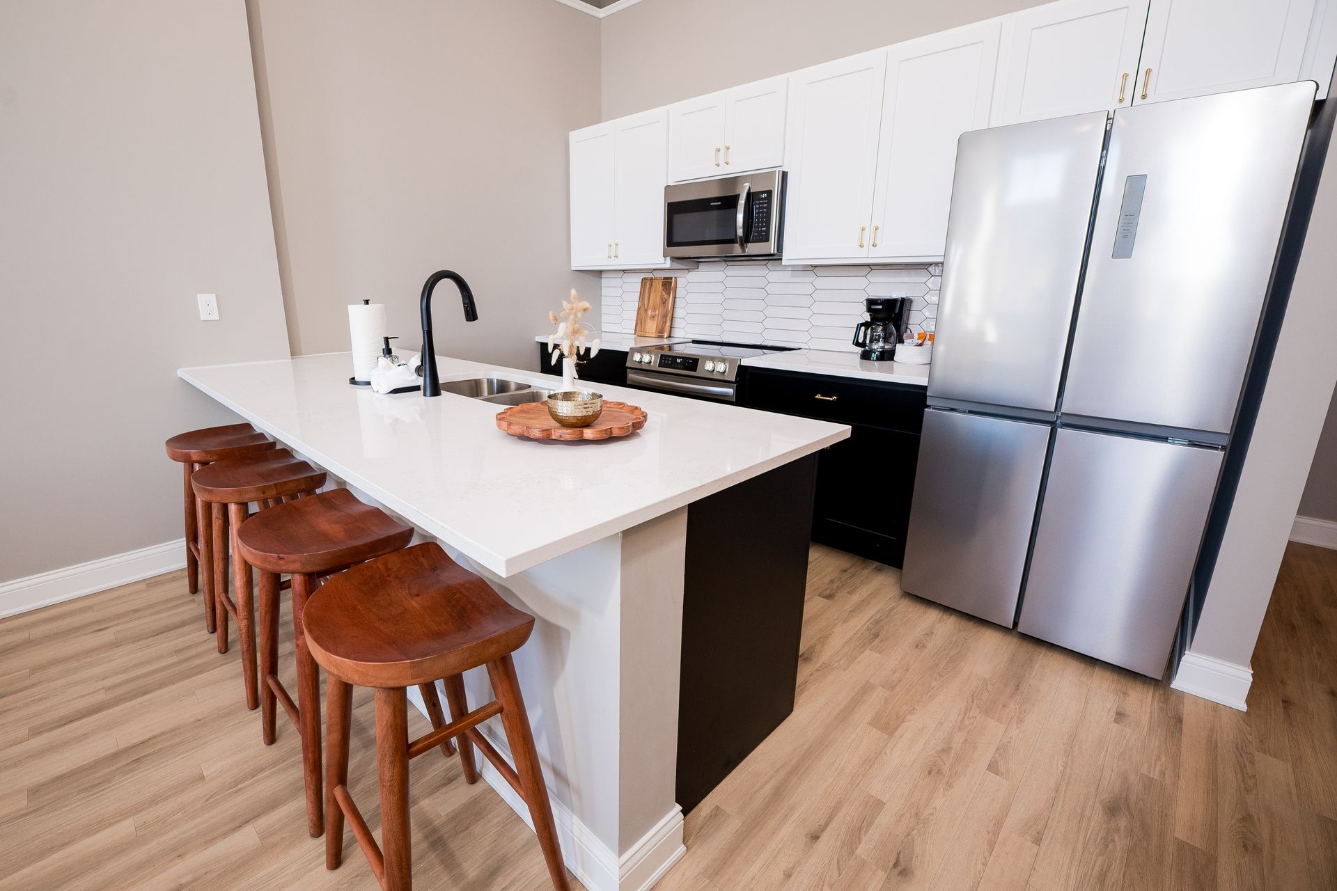Modern kitchen with white island, wooden stools, stainless appliances, and light wood floors