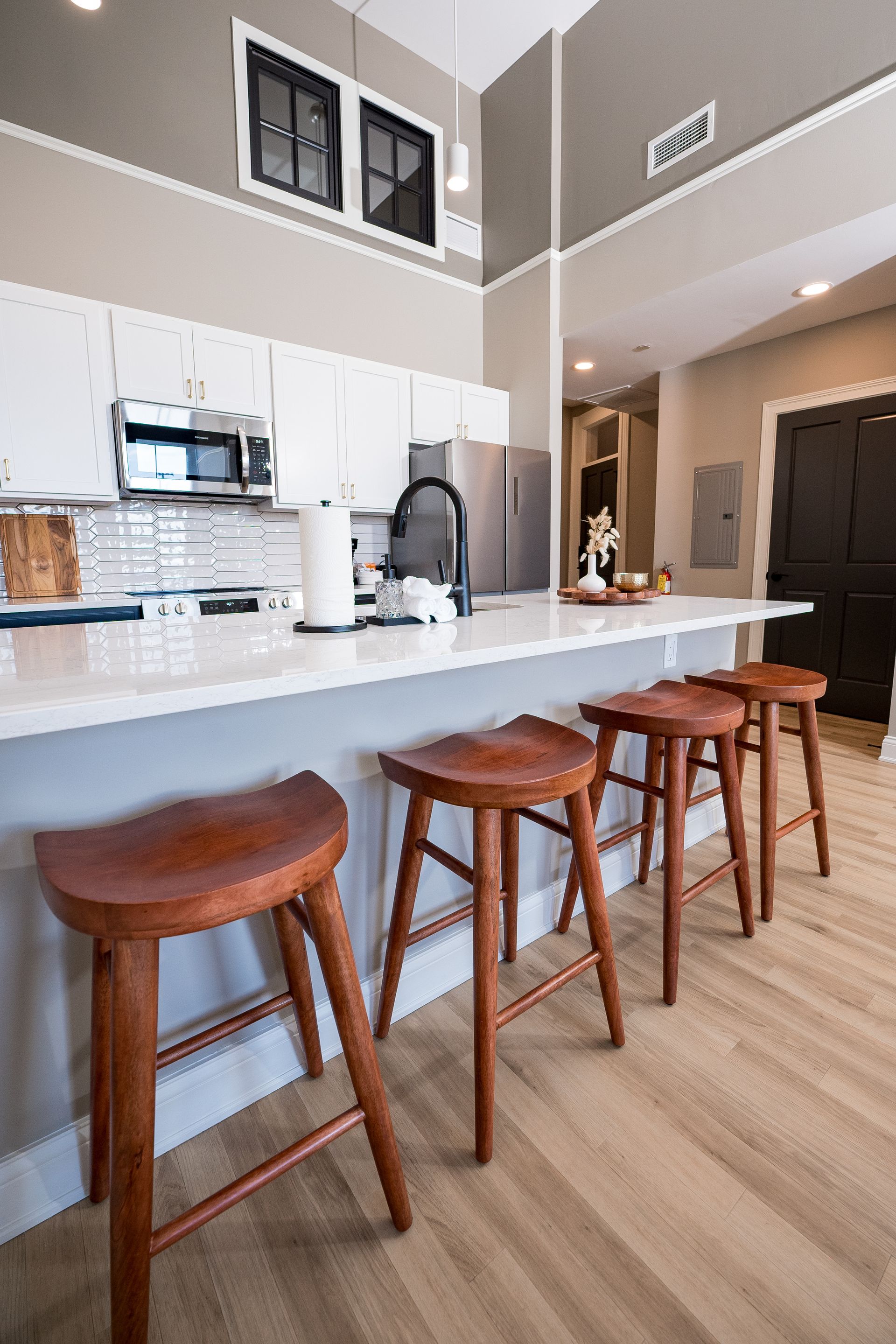 Modern kitchen with white island, three wooden stools, and high ceilings