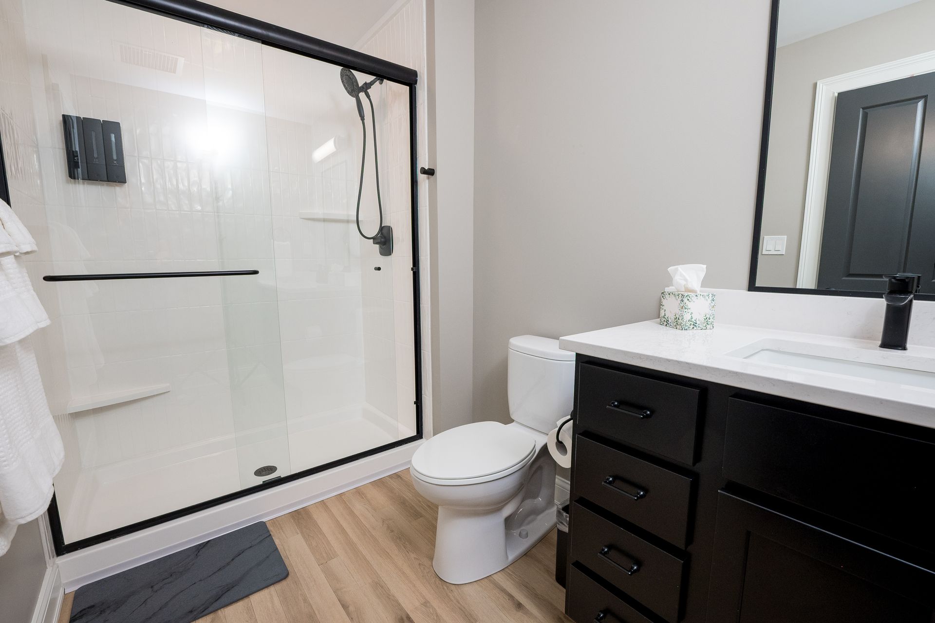 Modern bathroom with walk-in glass shower, toilet, and dark vanity with sink.