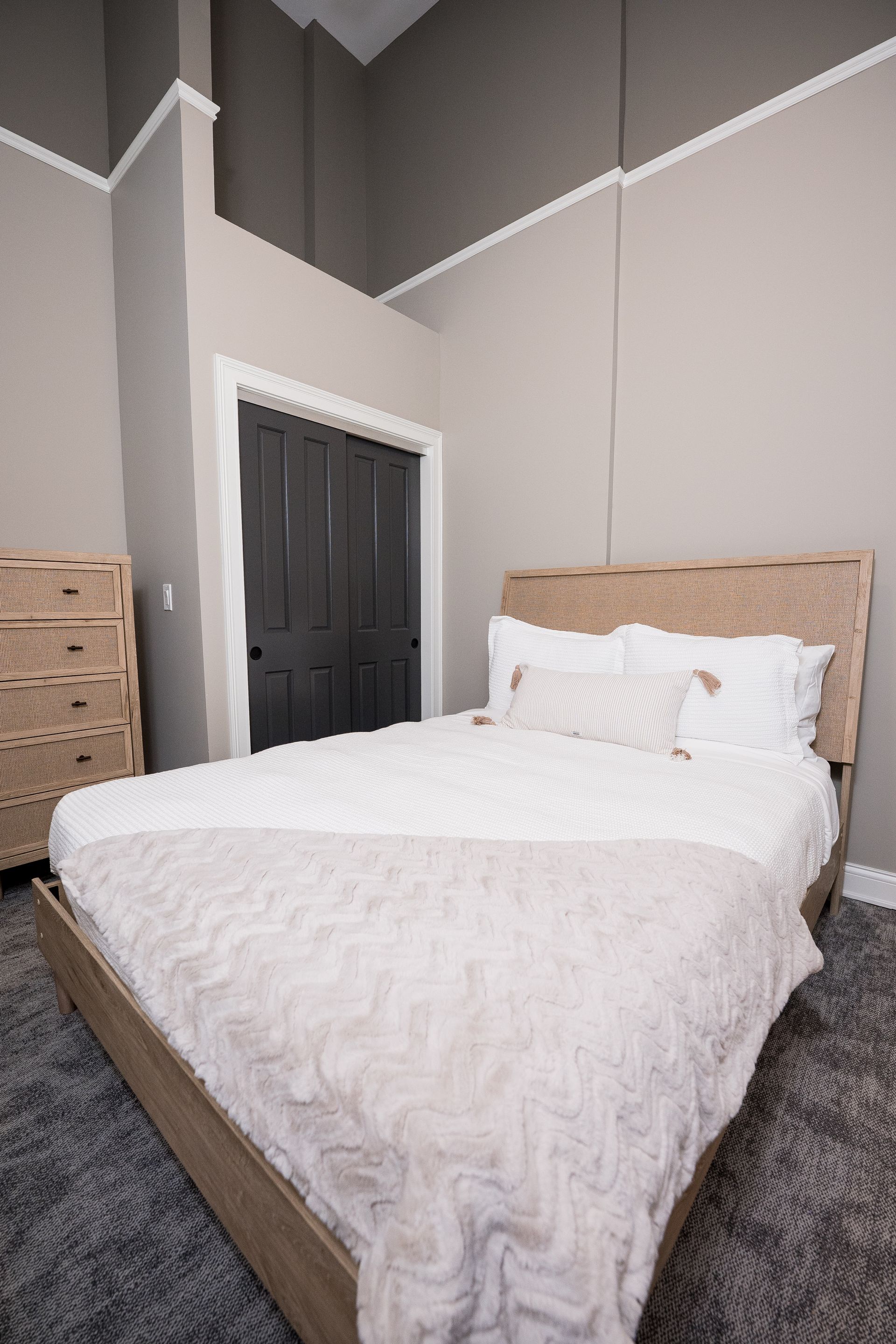 Cozy bedroom with a neatly made white bed, wicker headboard, and tall gray walls