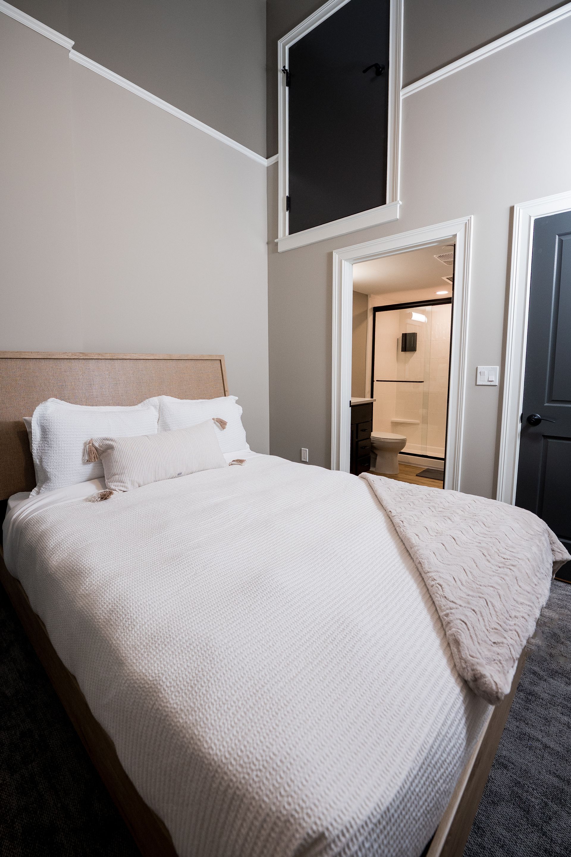 Small bedroom with a made bed, white bedding, beige headboard, and an open doorway to a bathroom.