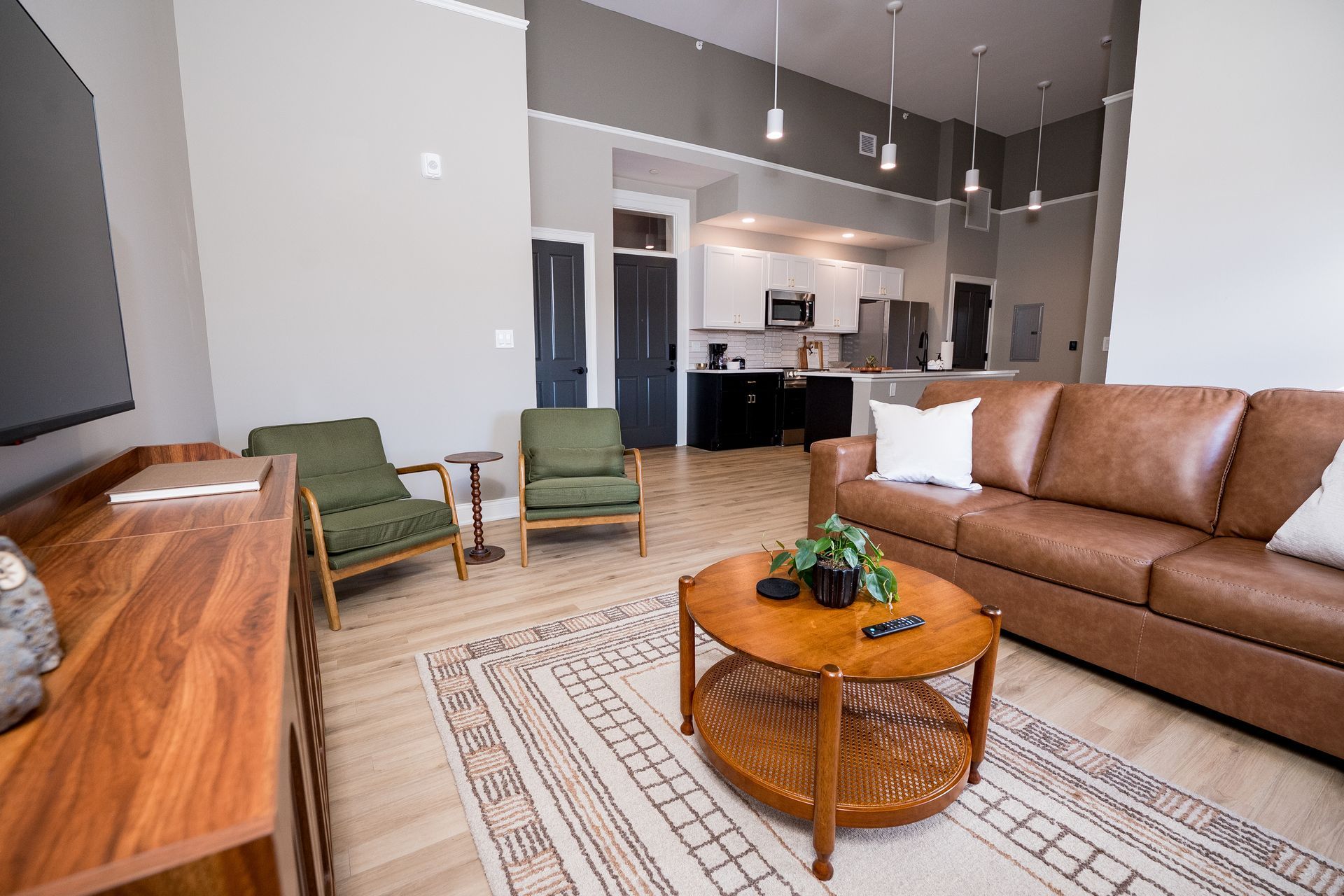 Modern living room with tan leather sofa, two green chairs, coffee table, and open kitchen area
