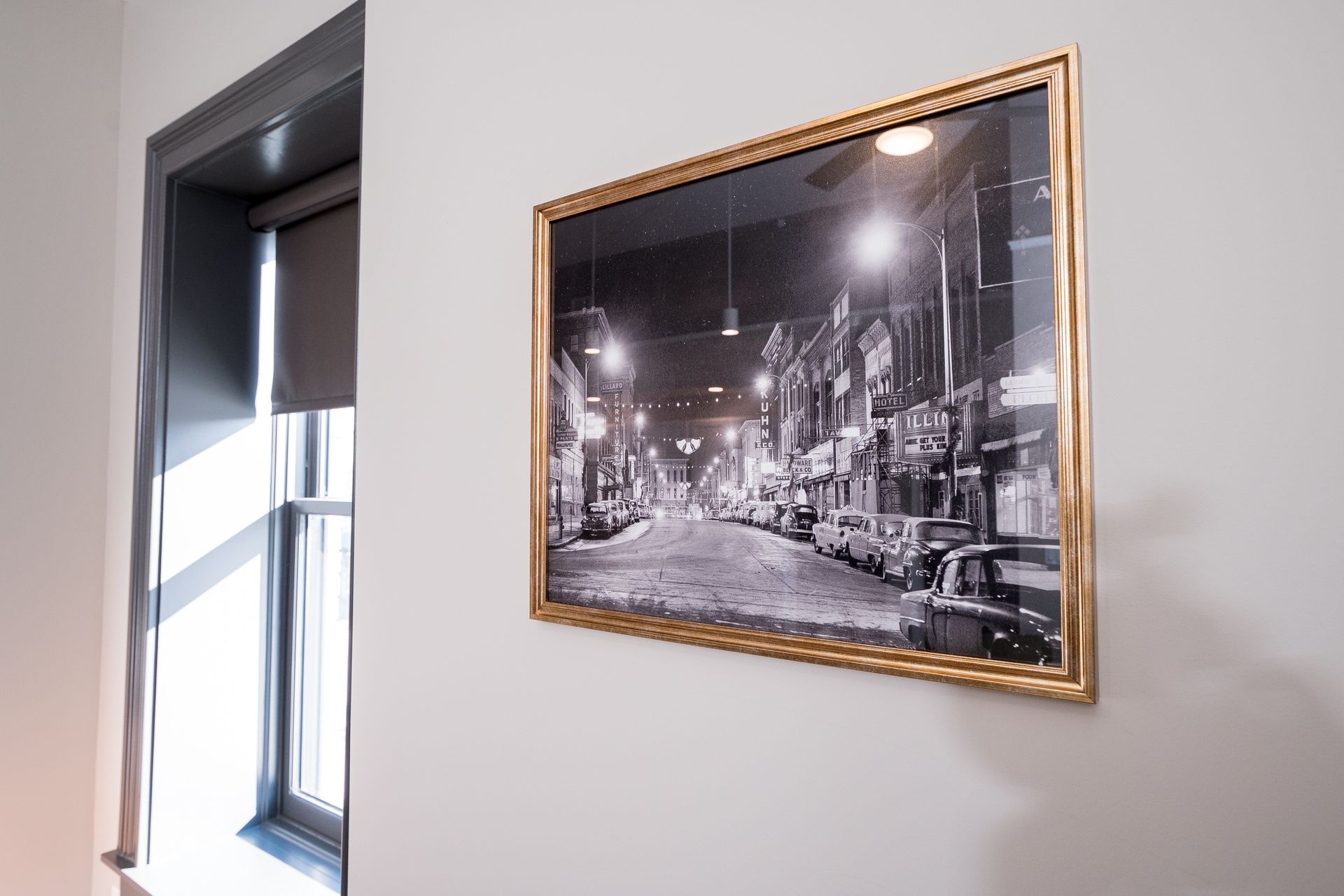 Framed black-and-white city street photo on a white wall beside a window