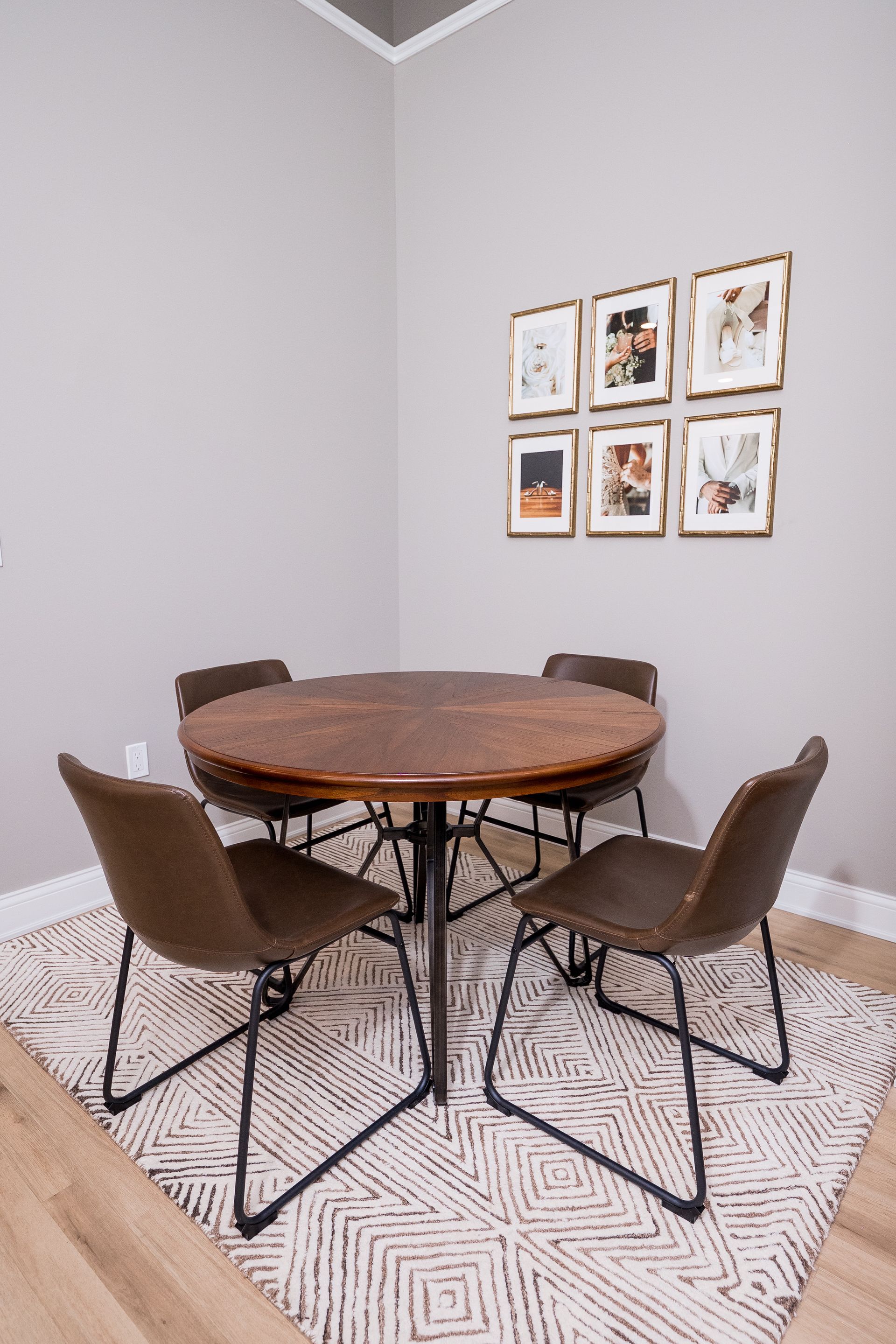 Small dining nook with a round wooden table, four chairs, patterned rug, and framed wall art.
