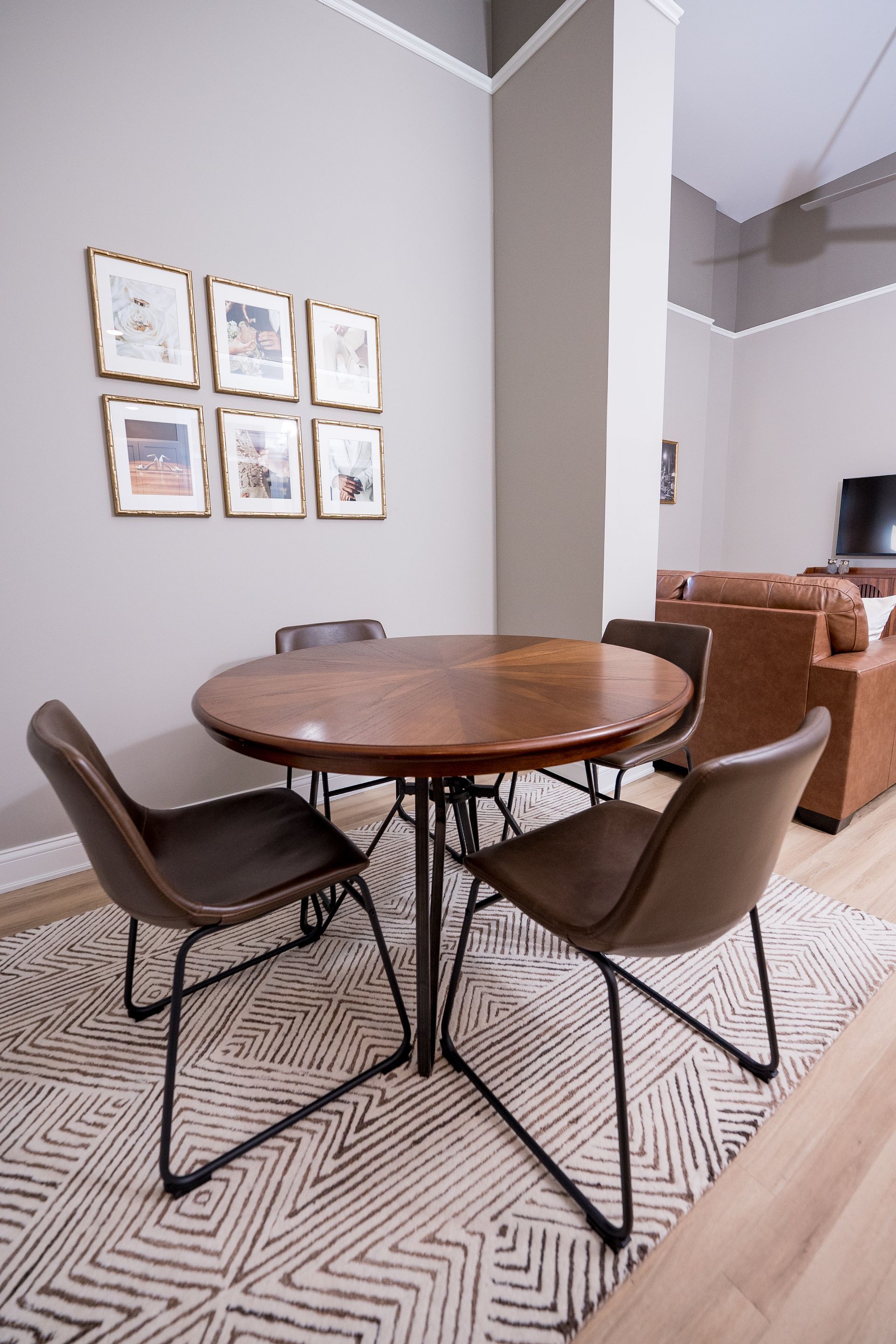 Round dining table with four brown chairs in a modern room with framed wall art.