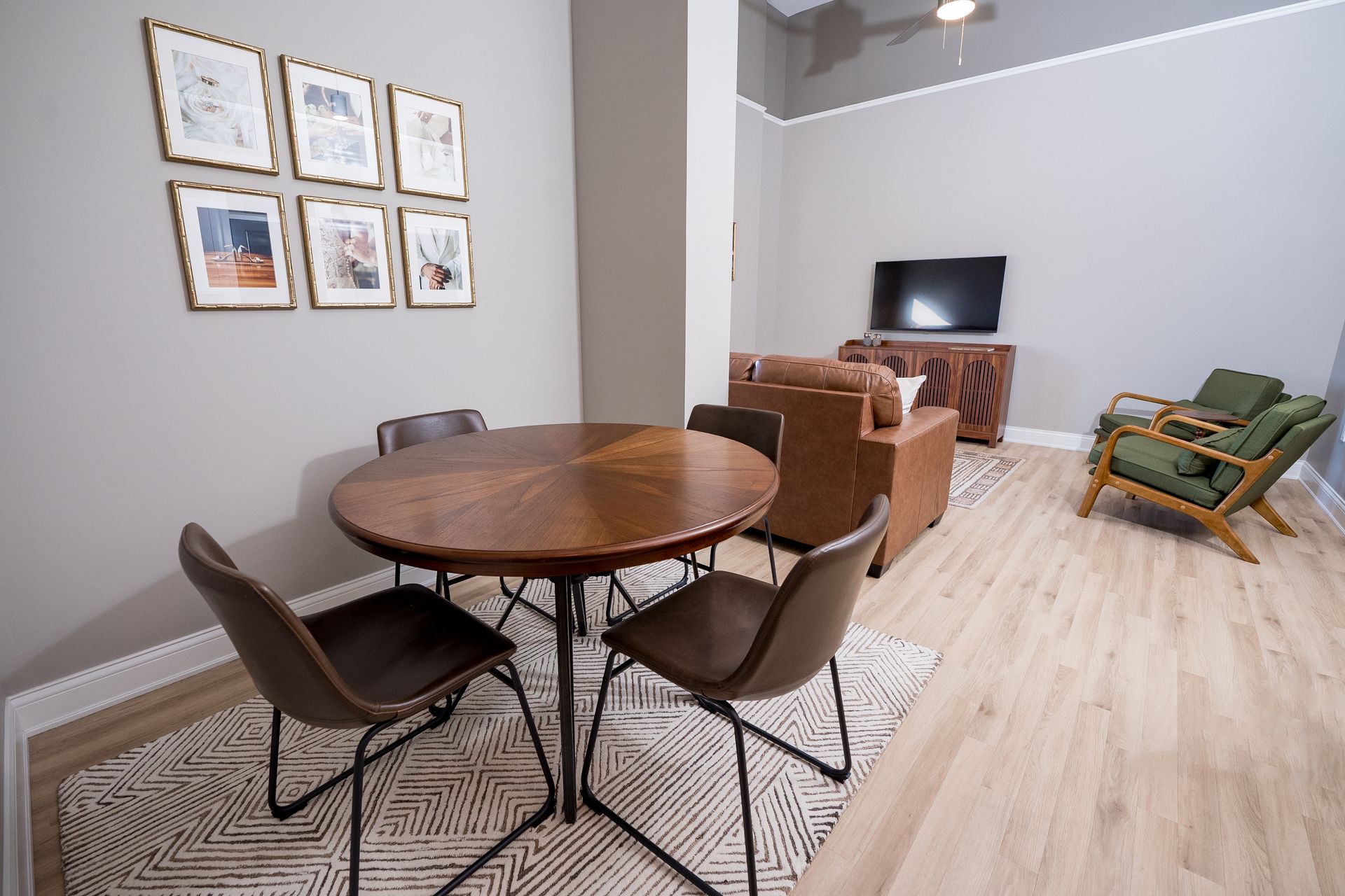 Modern living room with round dining table, framed wall art, TV, and green lounge chair