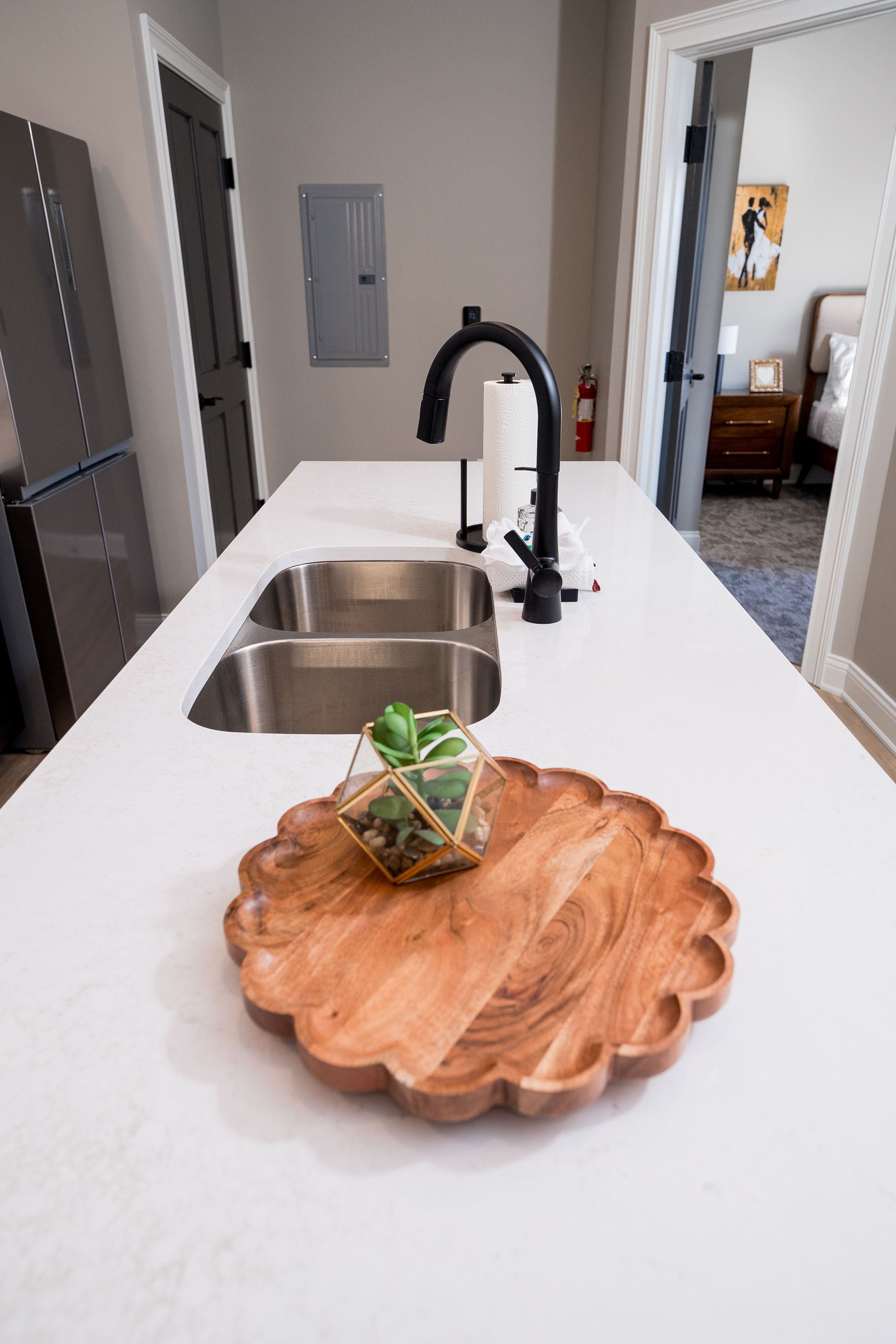 Bright kitchen island with stainless sink, black faucet, and wooden tray with plant centerpiece