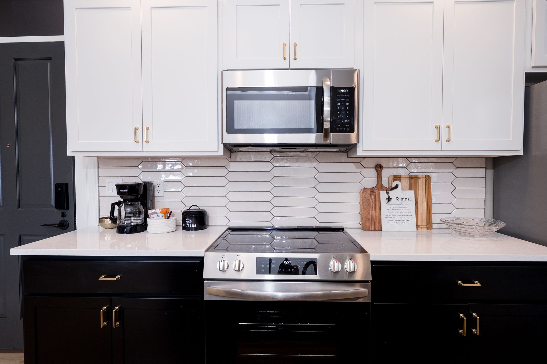 Modern kitchen with black-and-white cabinets, stainless steel appliances, and countertop coffee maker