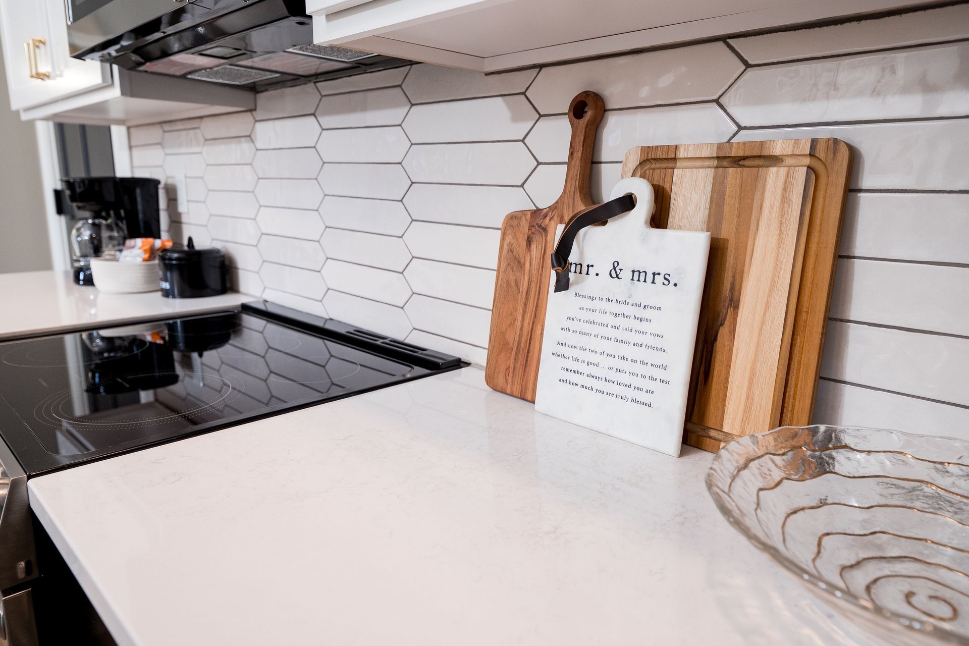 Modern kitchen countertop with stovetop, hex tile backsplash, and wooden cutting boards on a white counter