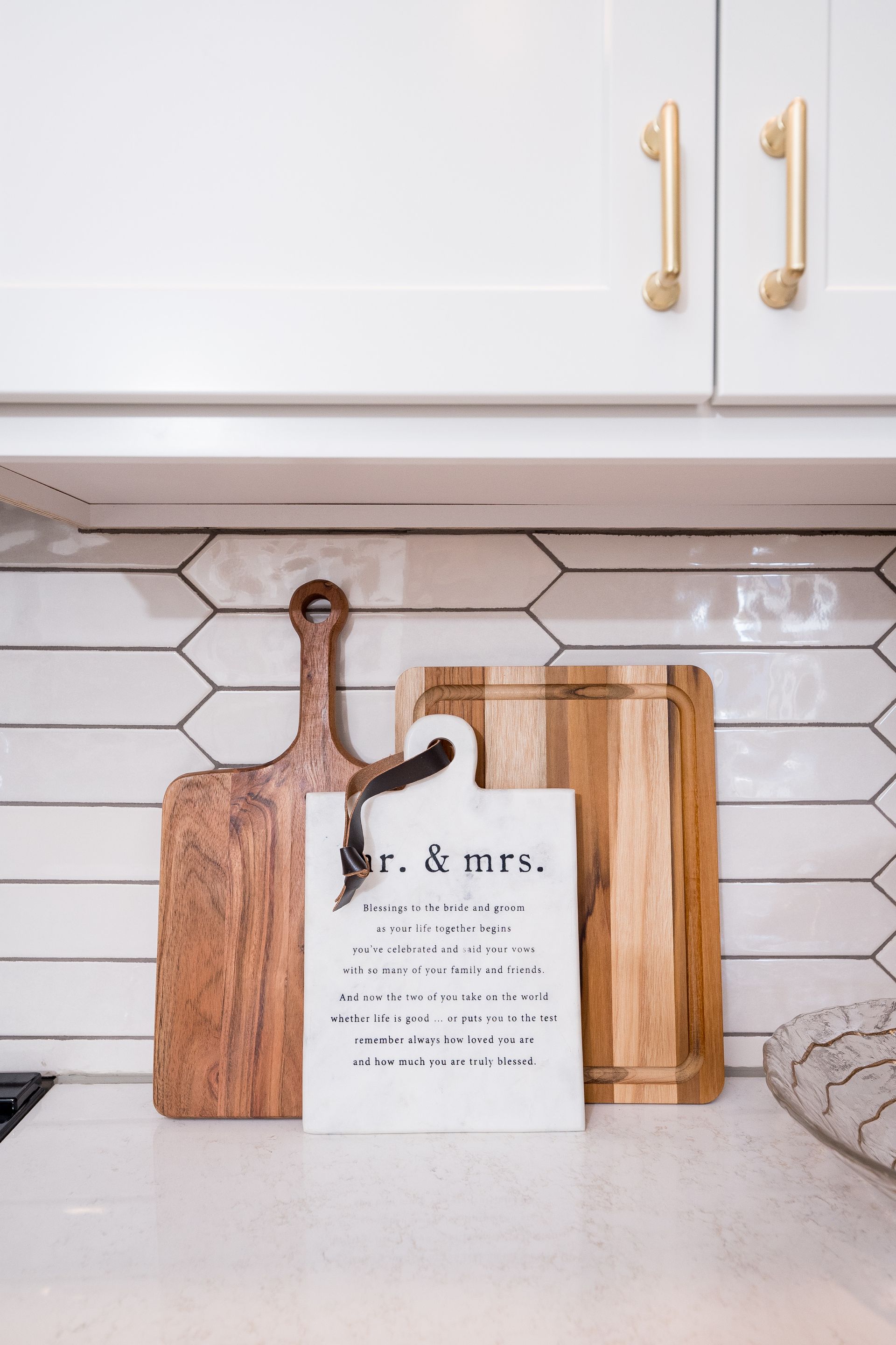 Cutting board with a wedding sign on a kitchen counter beneath white cabinets