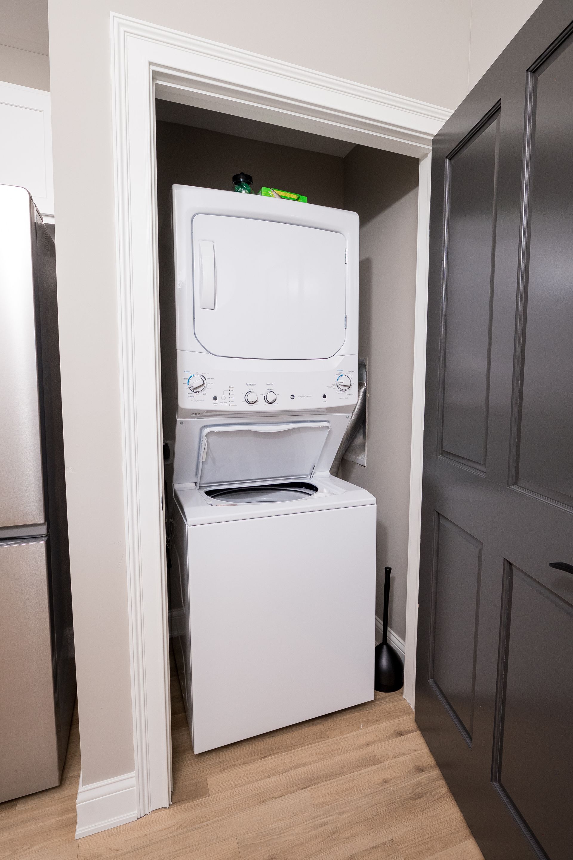 Stacked washer and dryer in a closet with dark gray doors, partially open.