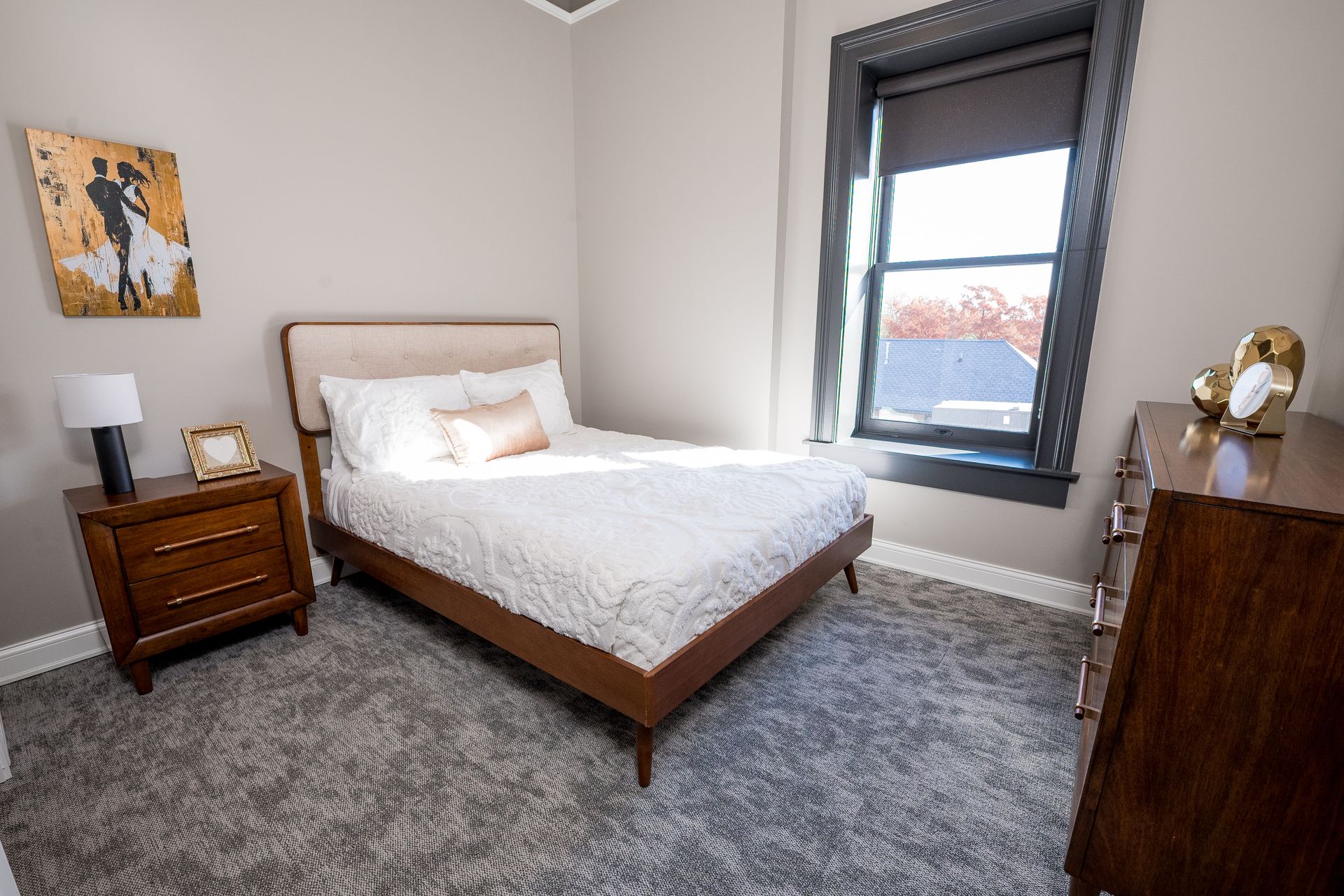 Bright bedroom with bed, nightstand, dresser, gray carpet, and window.