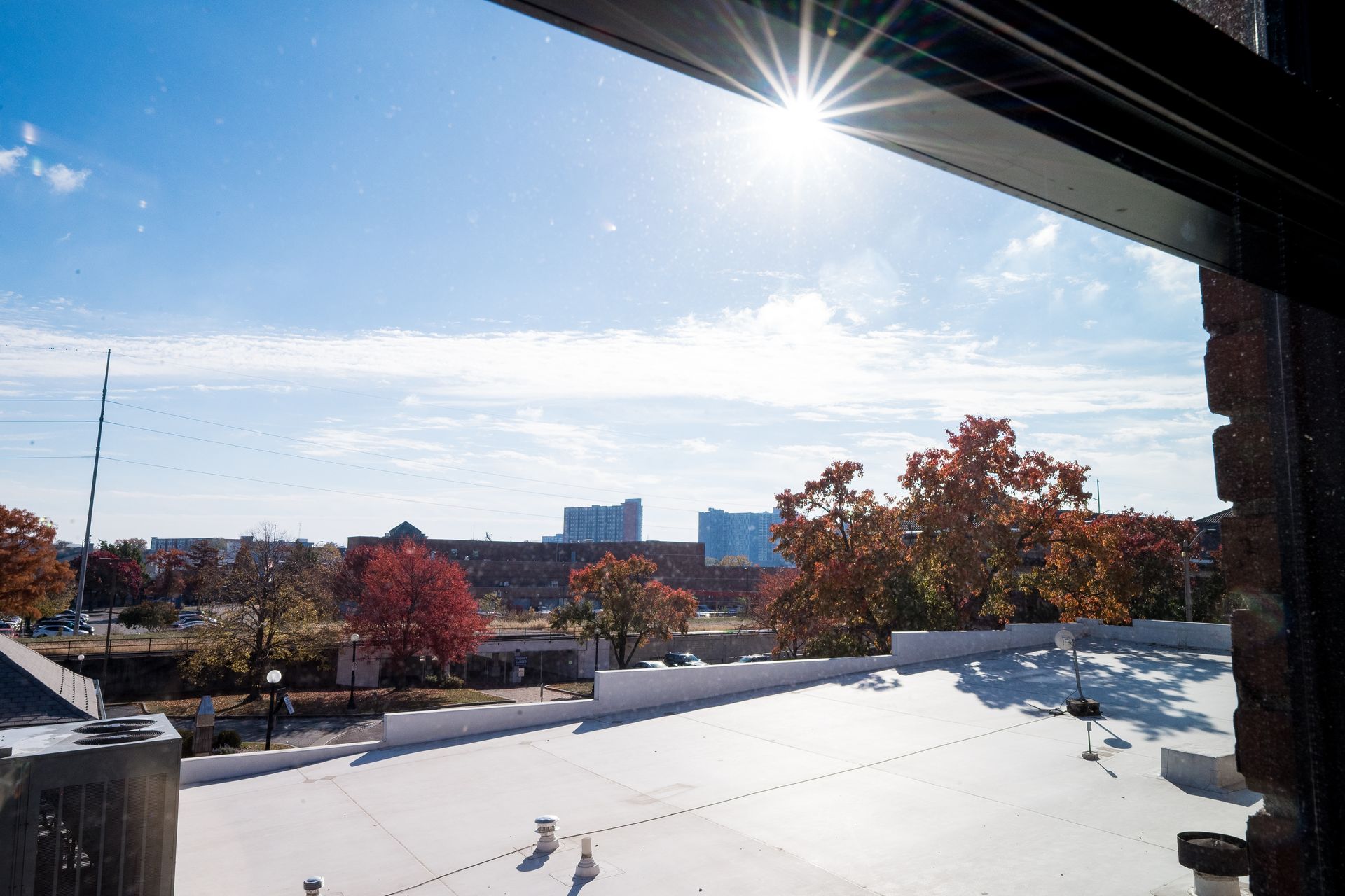 Snow-covered rooftop terrace with autumn trees and city buildings under a bright sun
