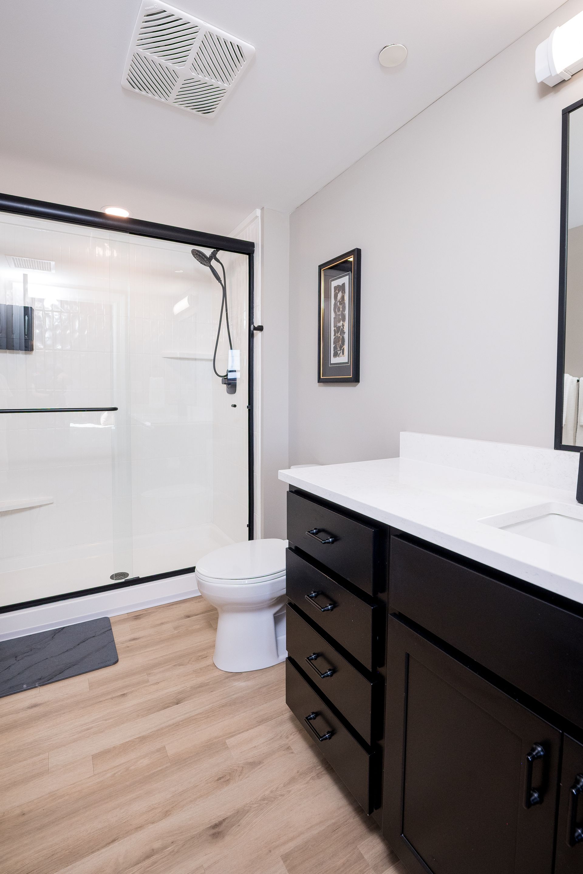 Modern bathroom with black vanity, white countertop, glass shower, and toilet.