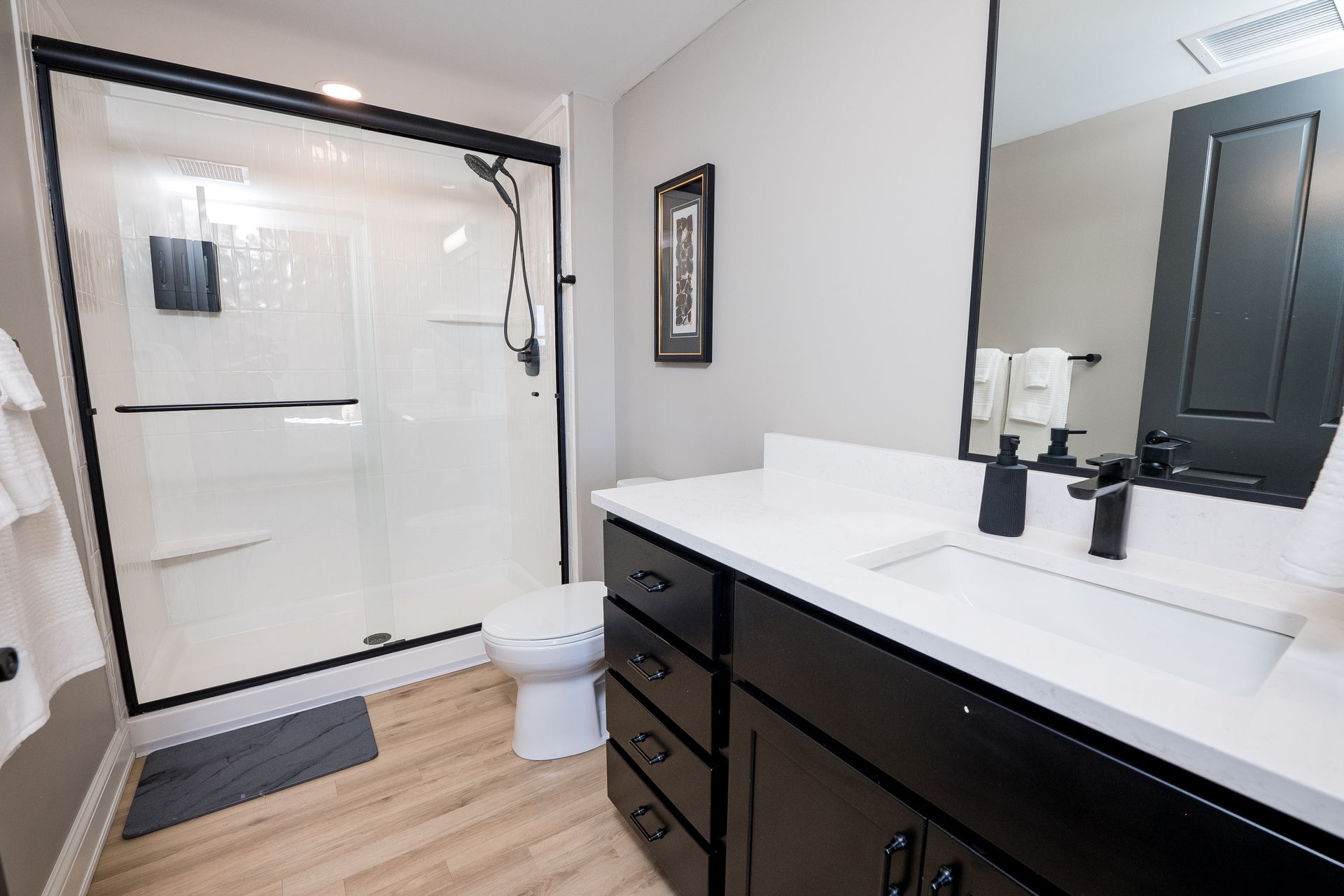 Bright bathroom with walk-in shower, black vanity, large mirror, and white walls