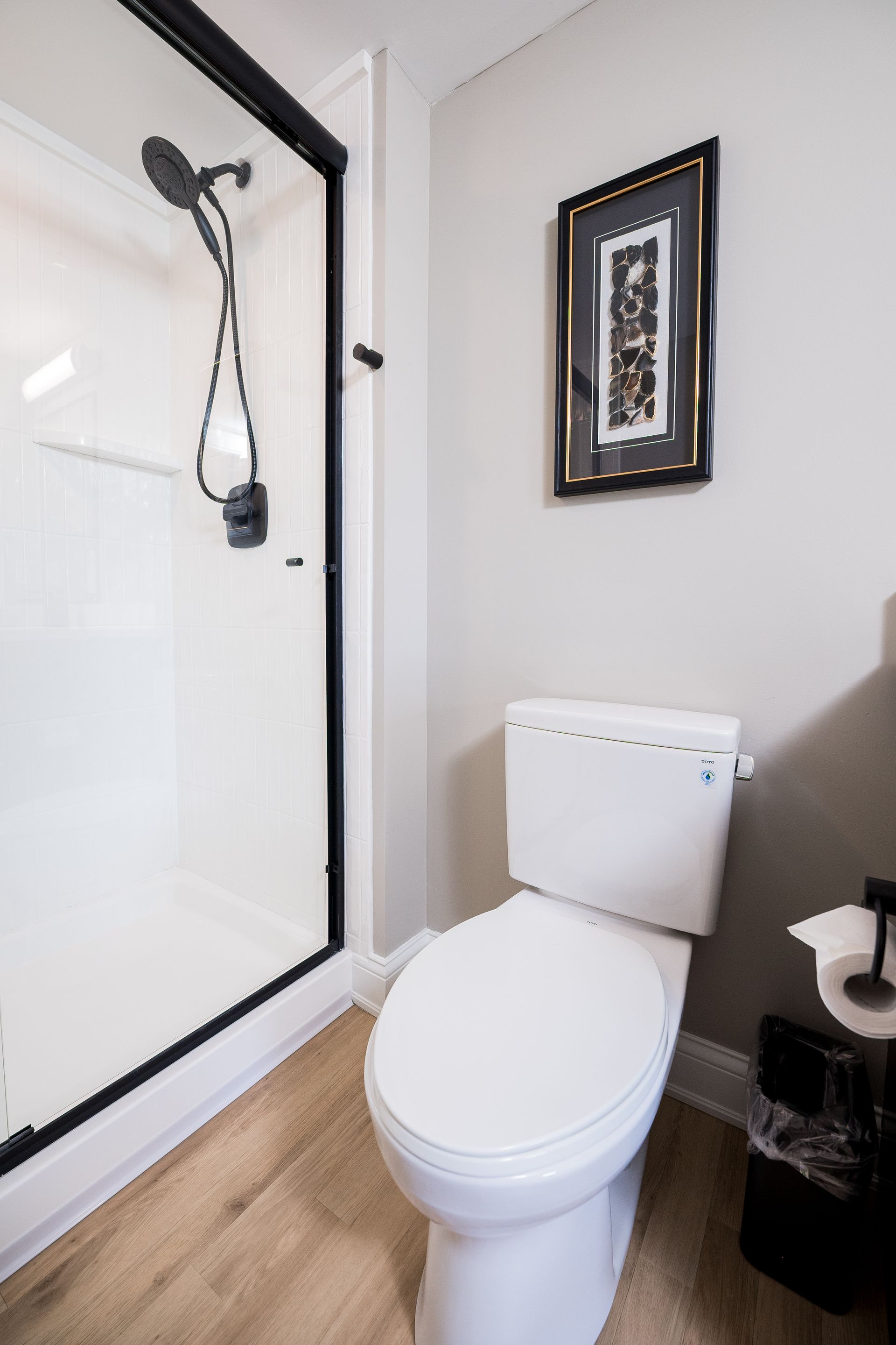 Small bathroom with white toilet, glass shower door, and framed wall art on a light wall