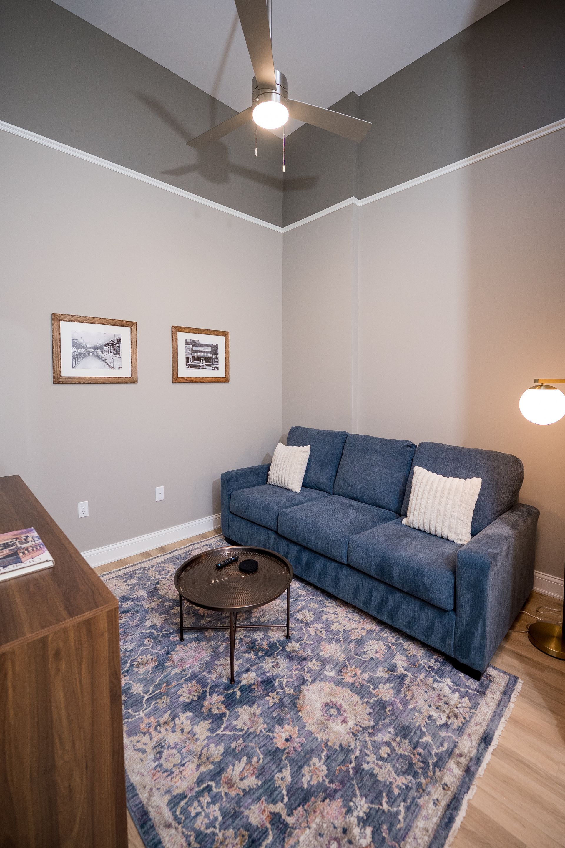 Small living room with blue sofa, patterned rug, coffee table, wall art, and ceiling fan.
