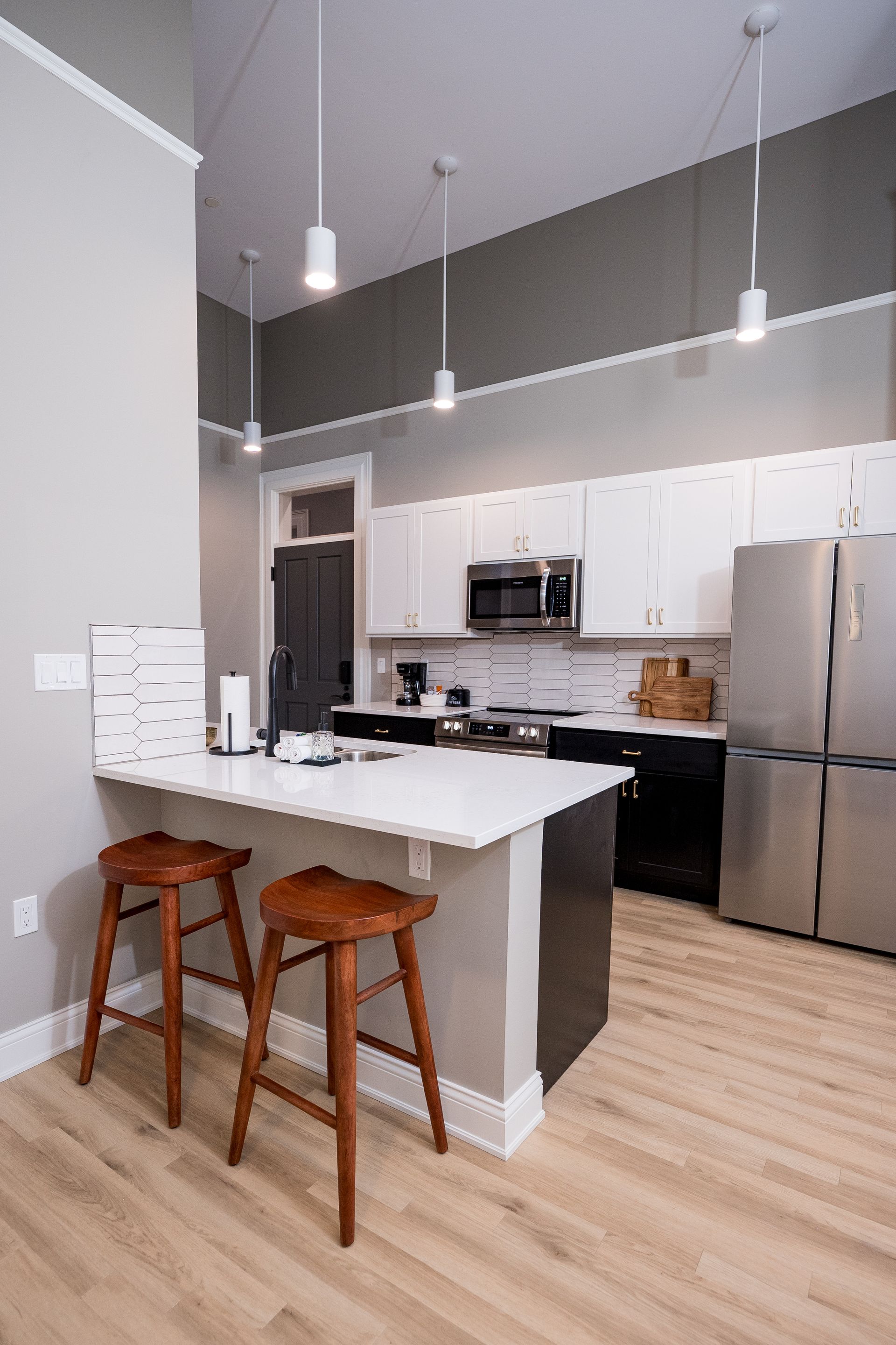 Modern kitchen with white island, wood stools, stainless steel appliances, and pendant lights