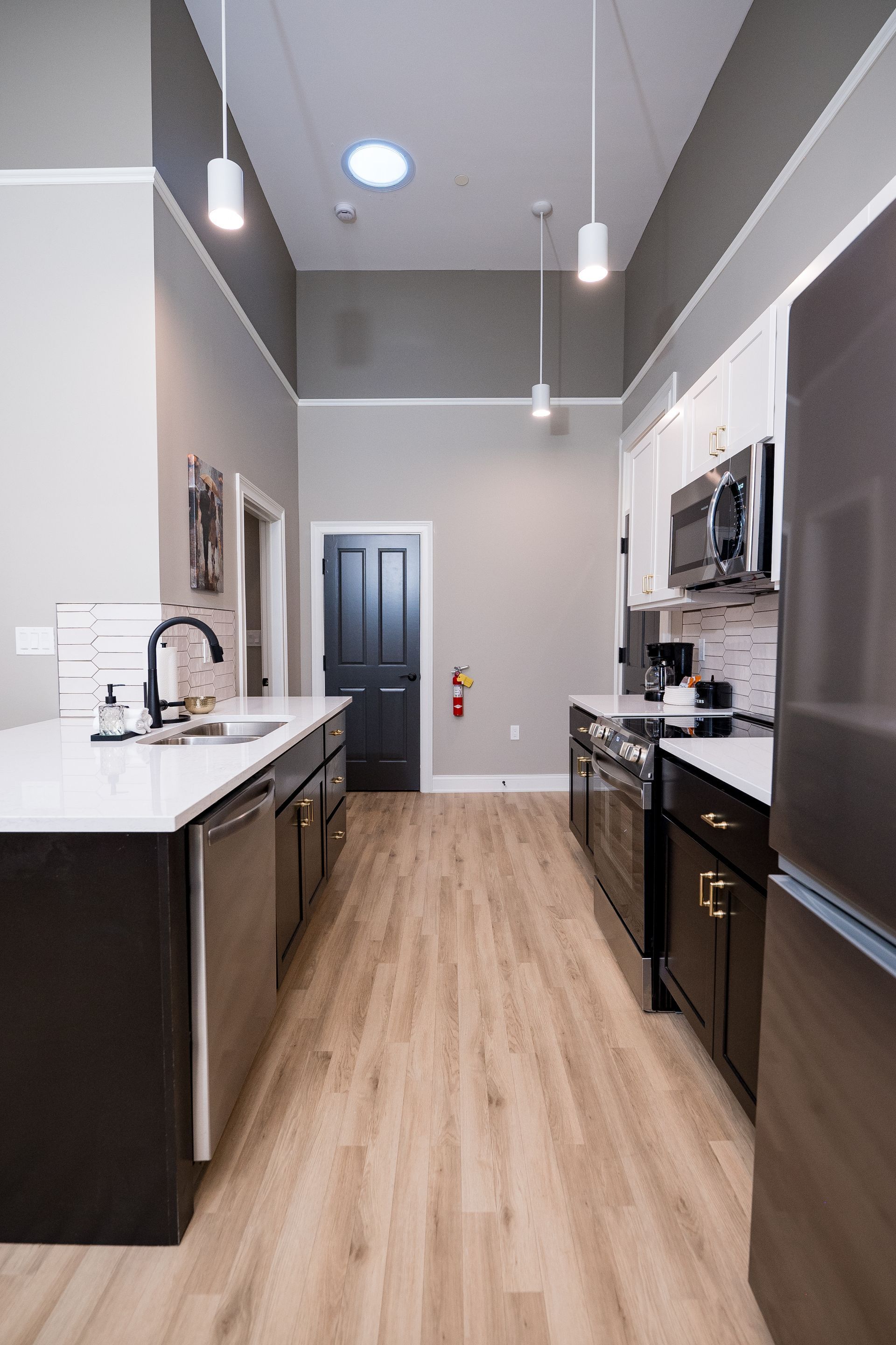 Modern kitchen with dark cabinets, white countertops, stainless appliances, and light wood flooring
