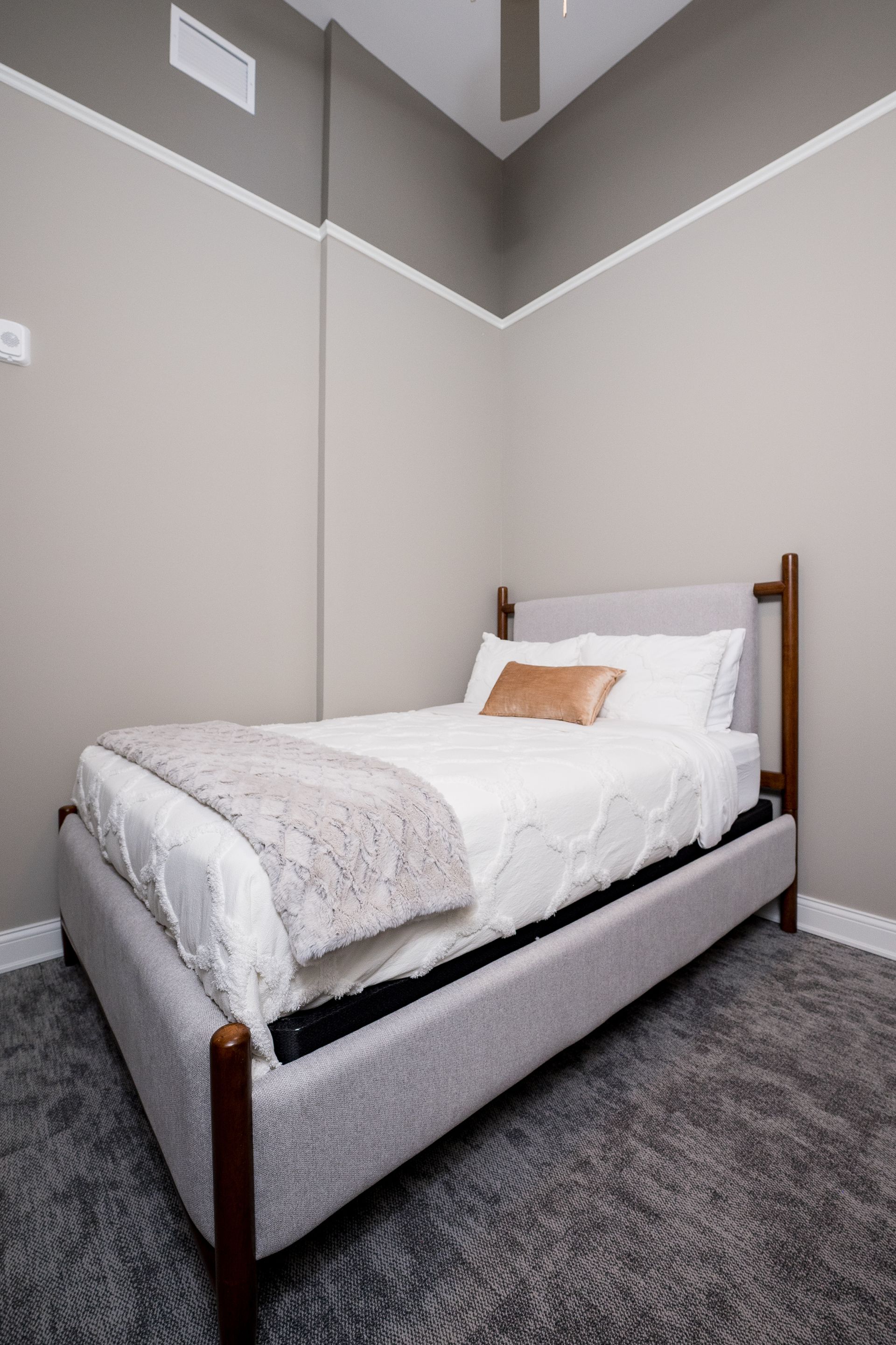 Small gray bedroom with a white bed, wooden posts, and a high vaulted ceiling.