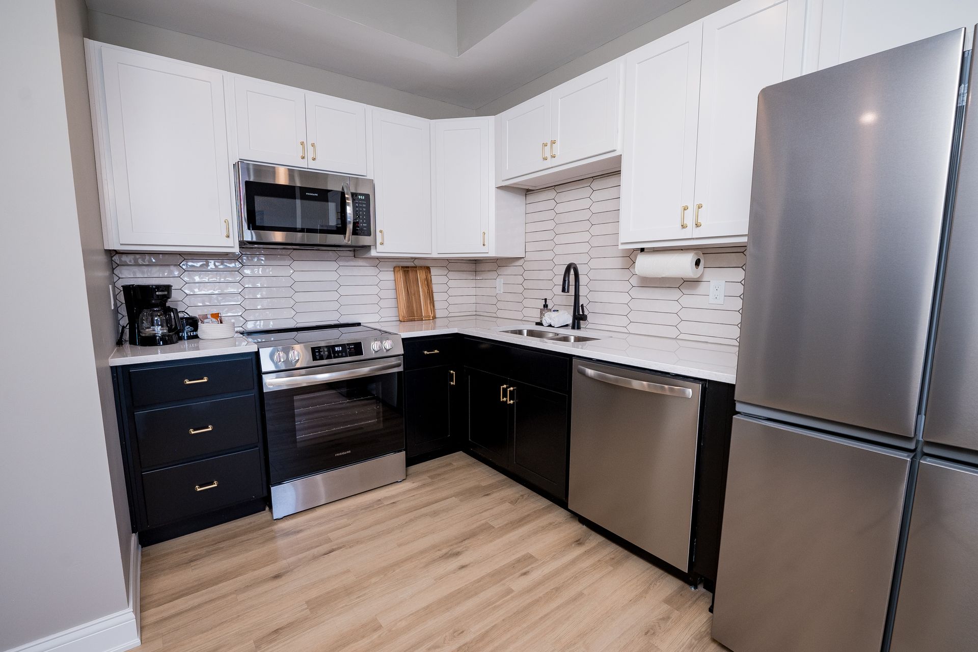 Modern kitchen with stainless steel appliances, dark lower cabinets, white upper cabinets, and light wood flooring