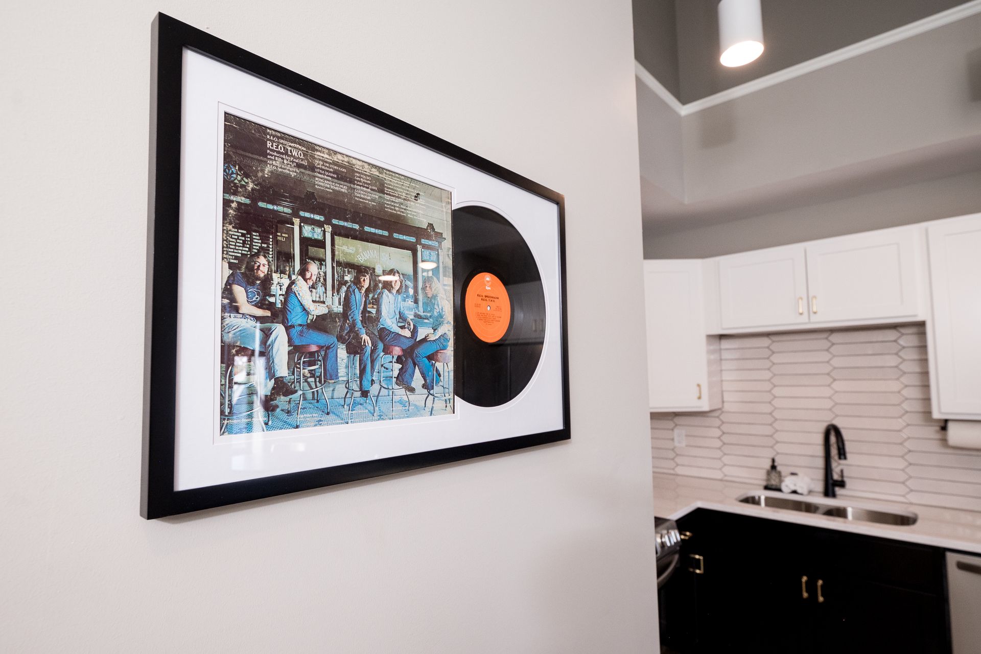 Framed vinyl record and album art on a white wall beside a modern kitchen