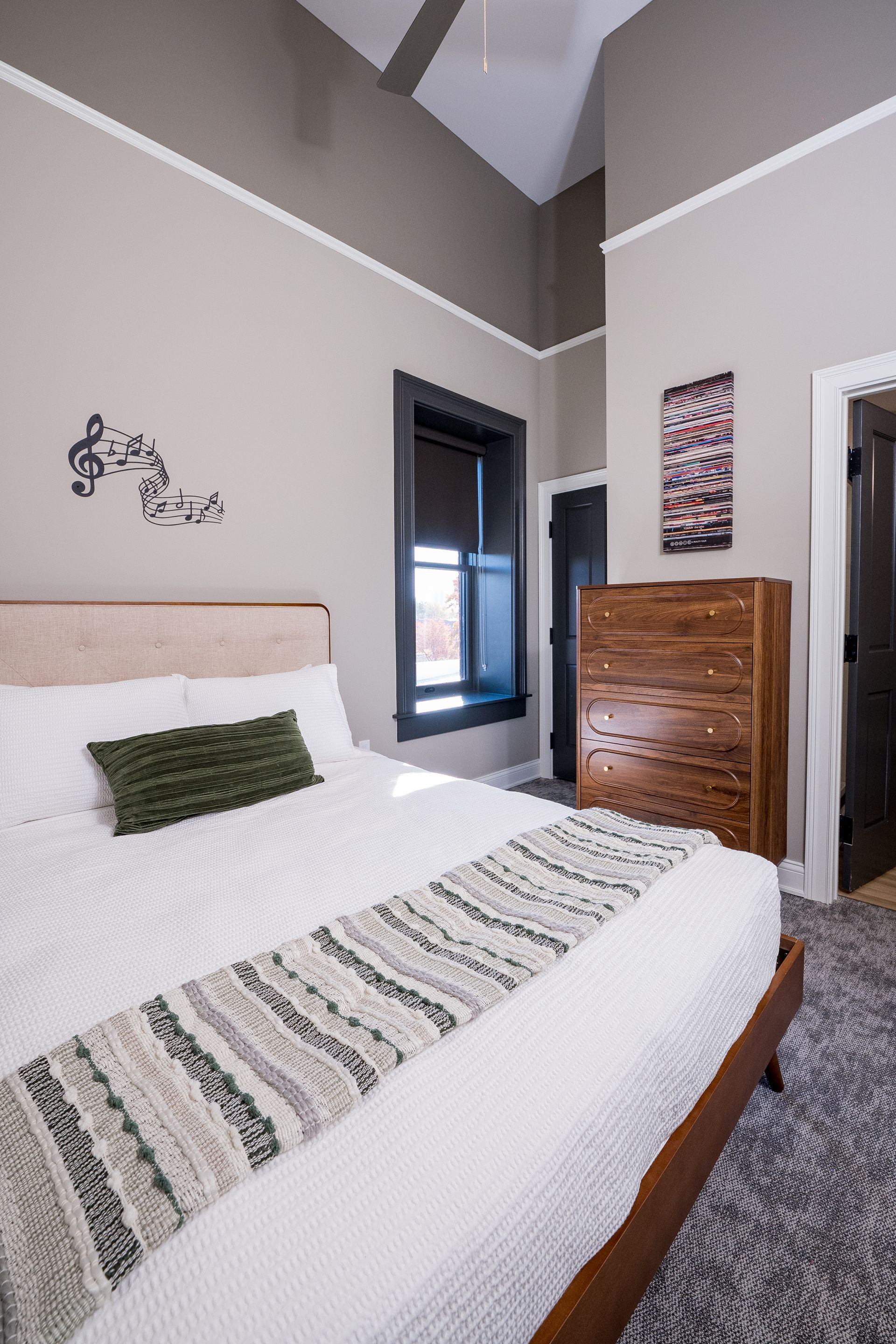 Bright bedroom with a bed, patterned runner, dresser, and open doorway to a bathroom