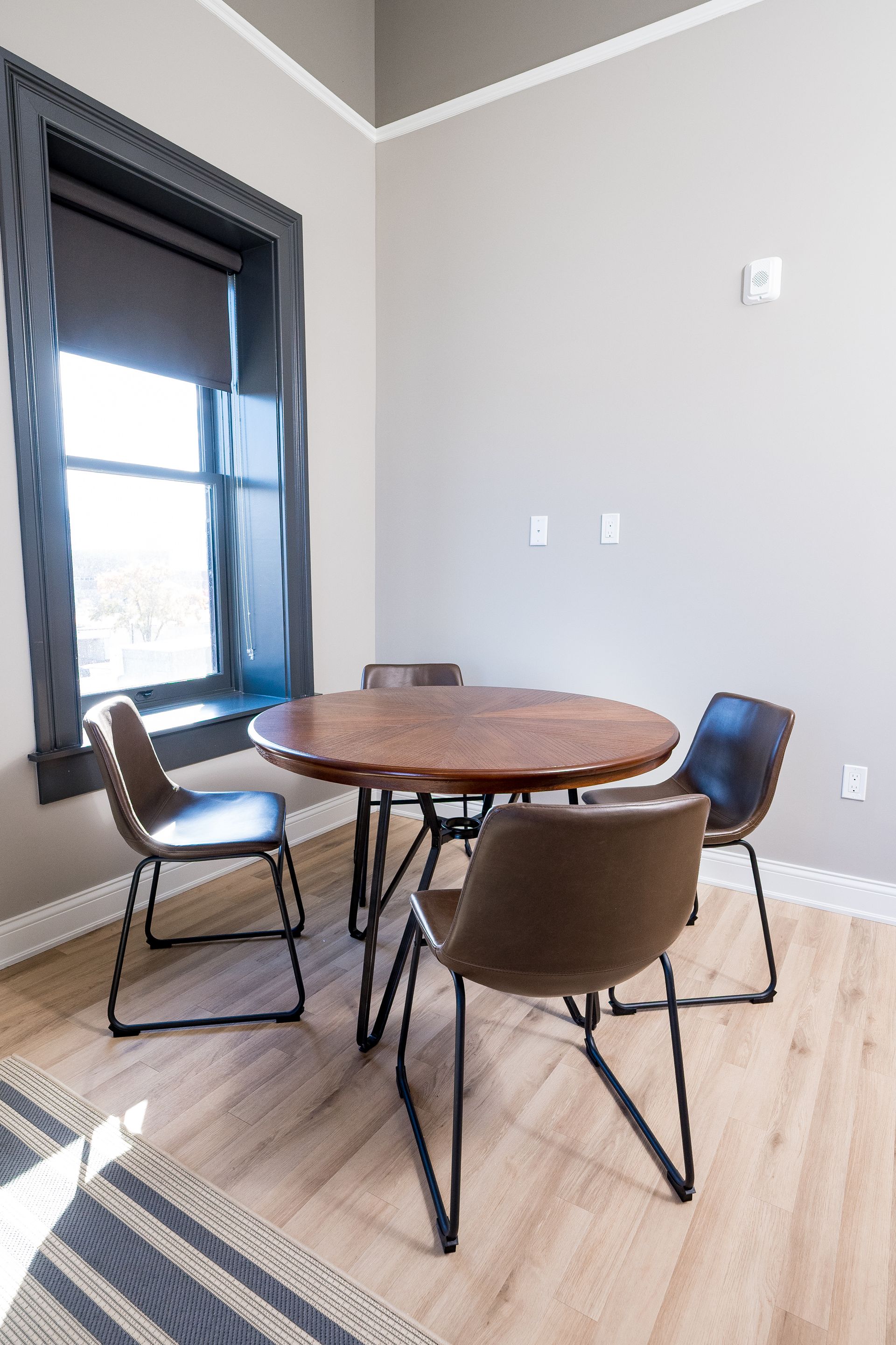 Small dining area with round wooden table and four chairs beside a window