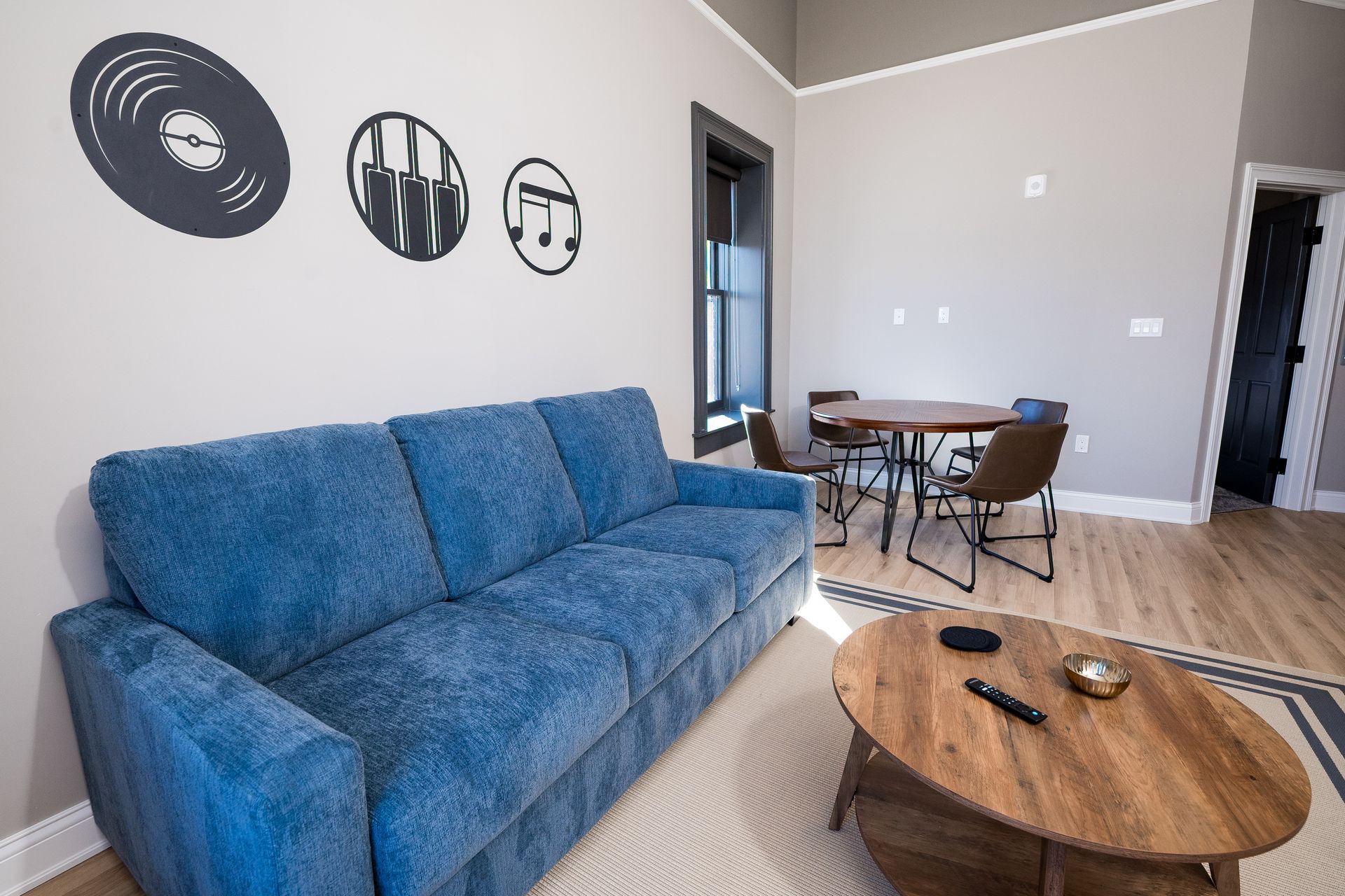 Blue couch in a modern living room with wall art, coffee table, and small dining area