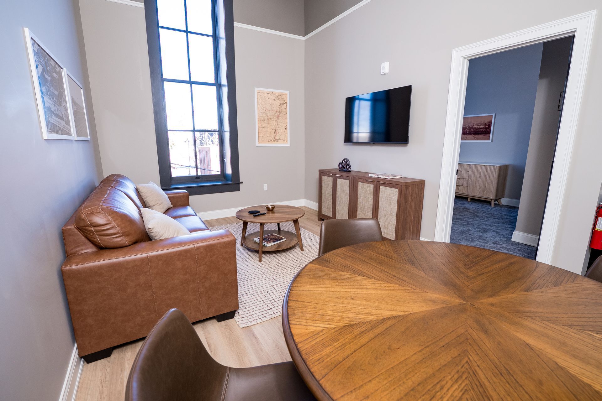 Modern living room with brown sofa, round wooden table, TV, and gray walls