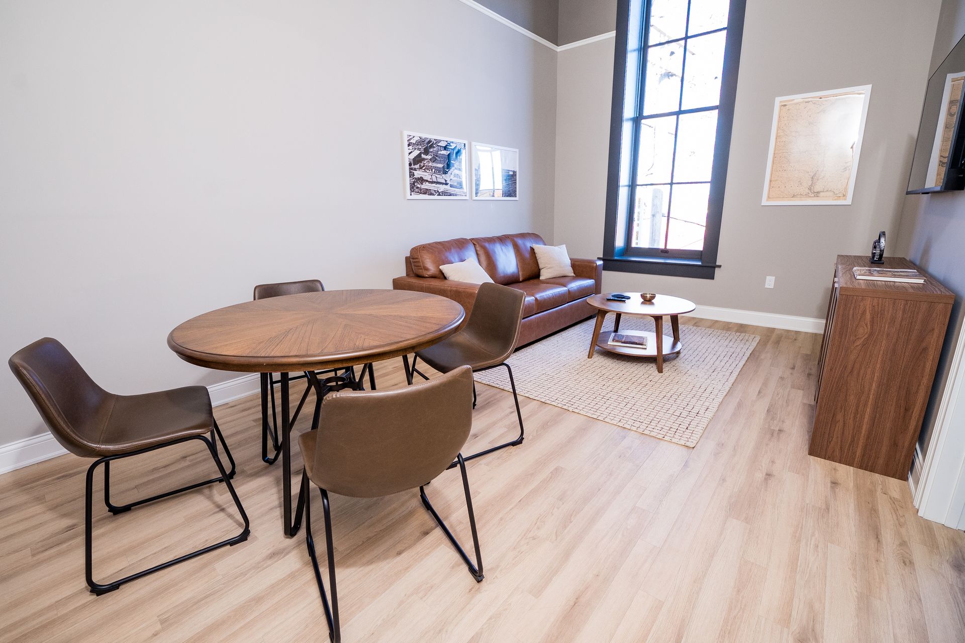 Modern living room with round wood table, chairs, sofa, rug, and tall window on gray walls