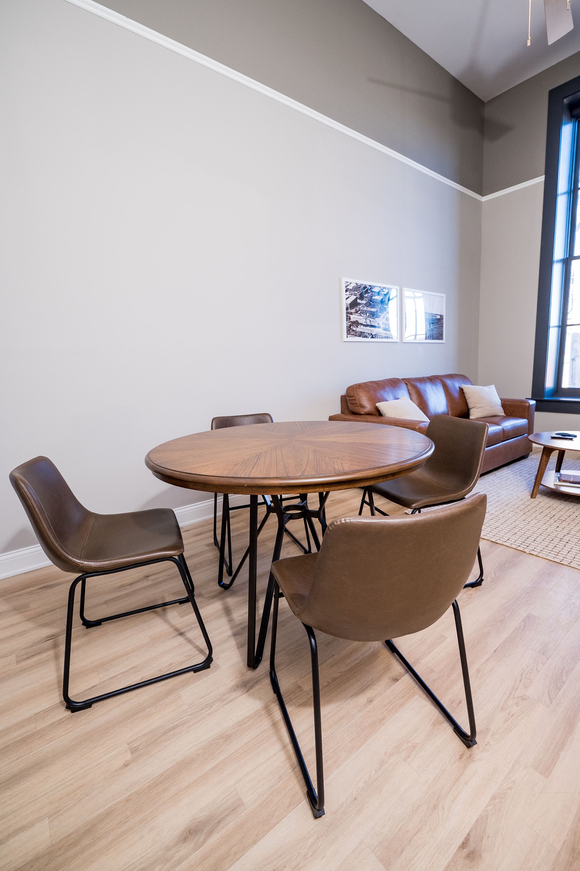 Round wooden table with four chairs in a bright modern lounge area with light wood floors.