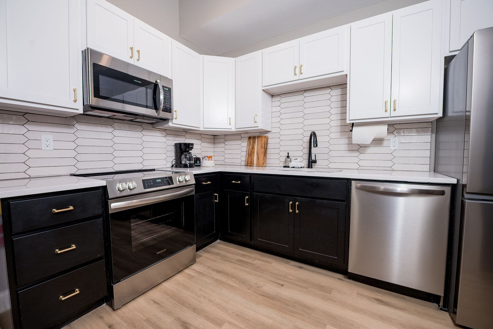Modern kitchen with white and black cabinets, stainless steel appliances, and light wood flooring