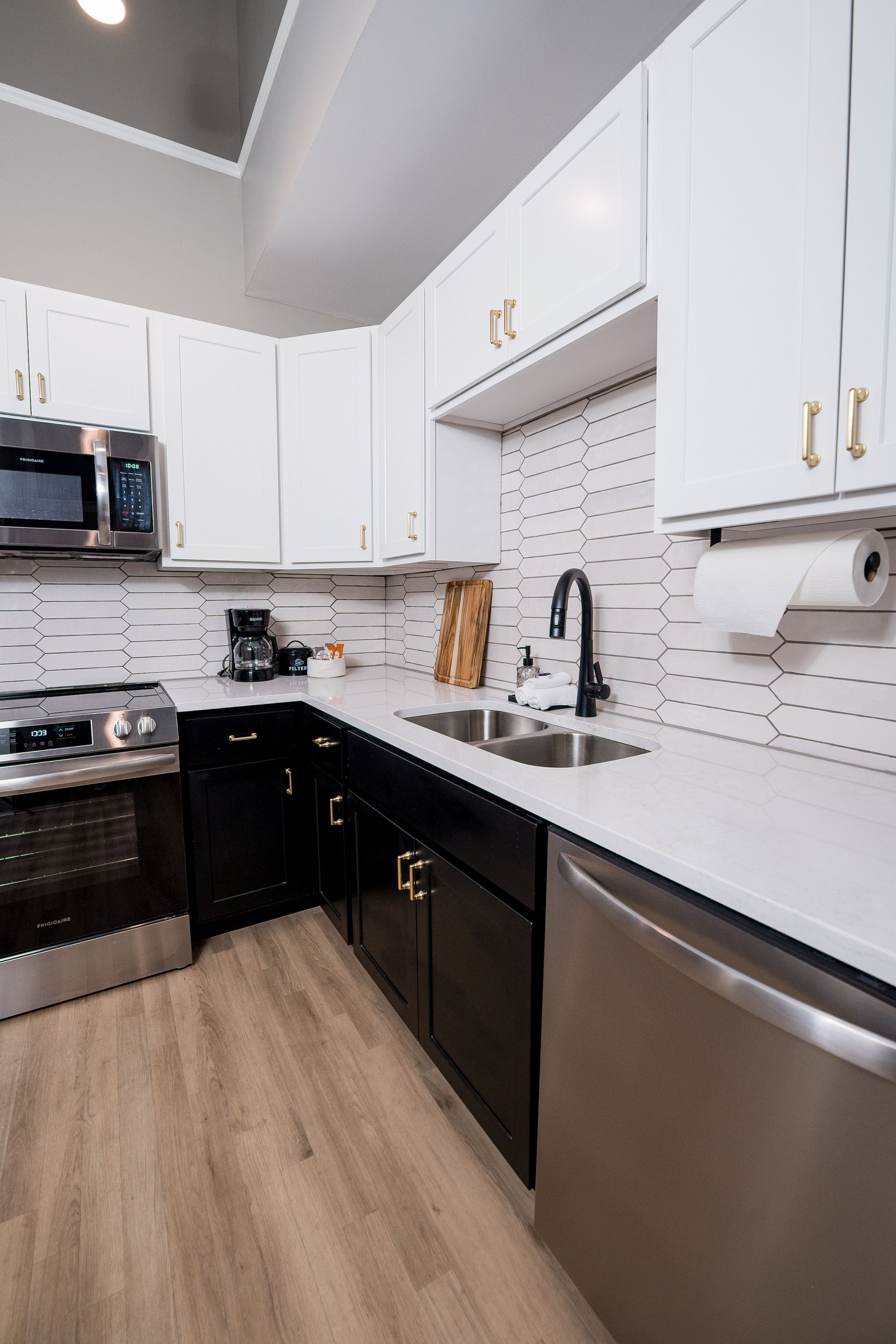 Modern kitchen with white cabinets, black appliances, and stainless steel sink on a light wood floor