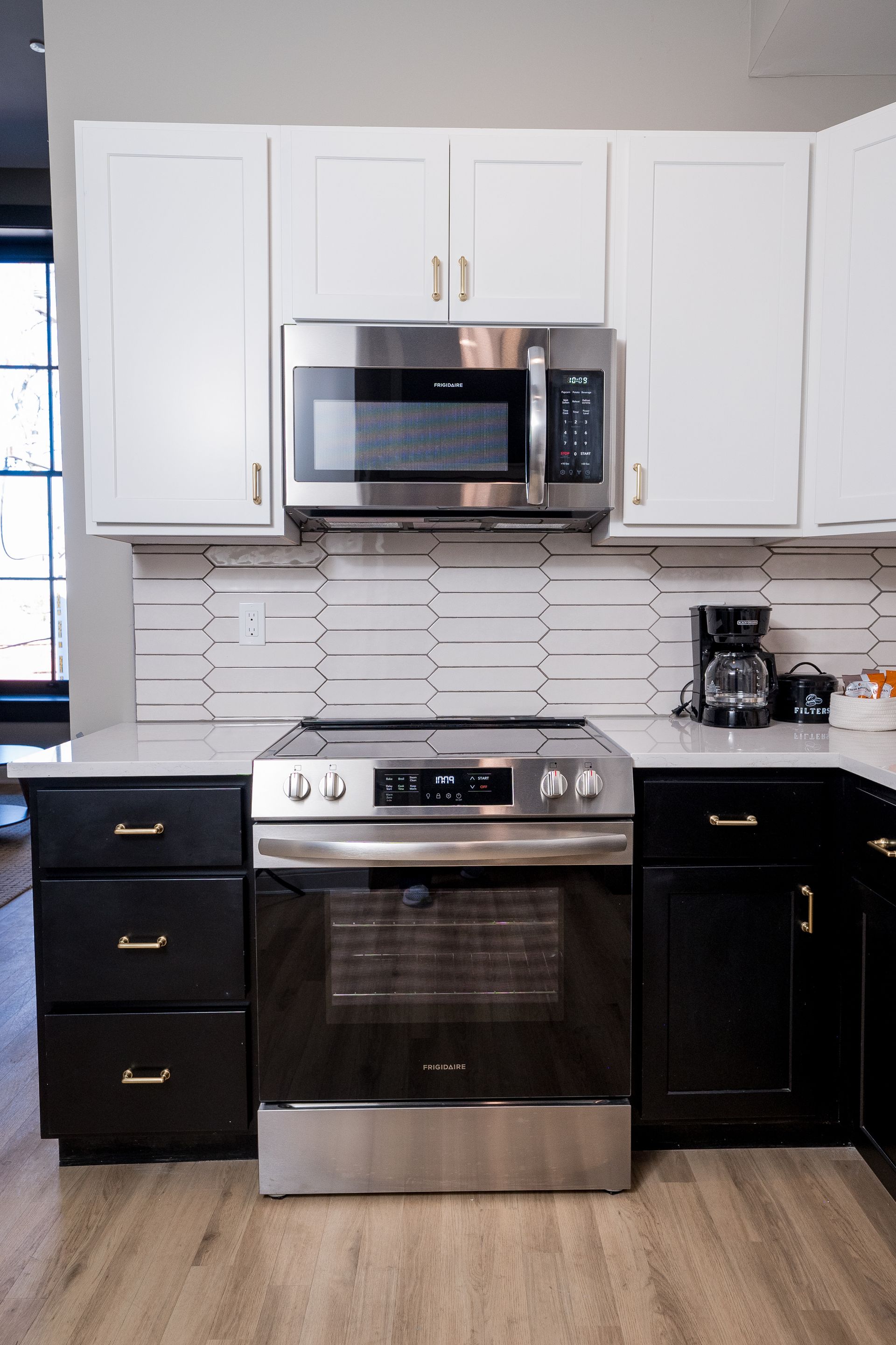 Modern kitchen with stainless steel stove and microwave, white upper cabinets, black lower cabinets, and coffee maker.
