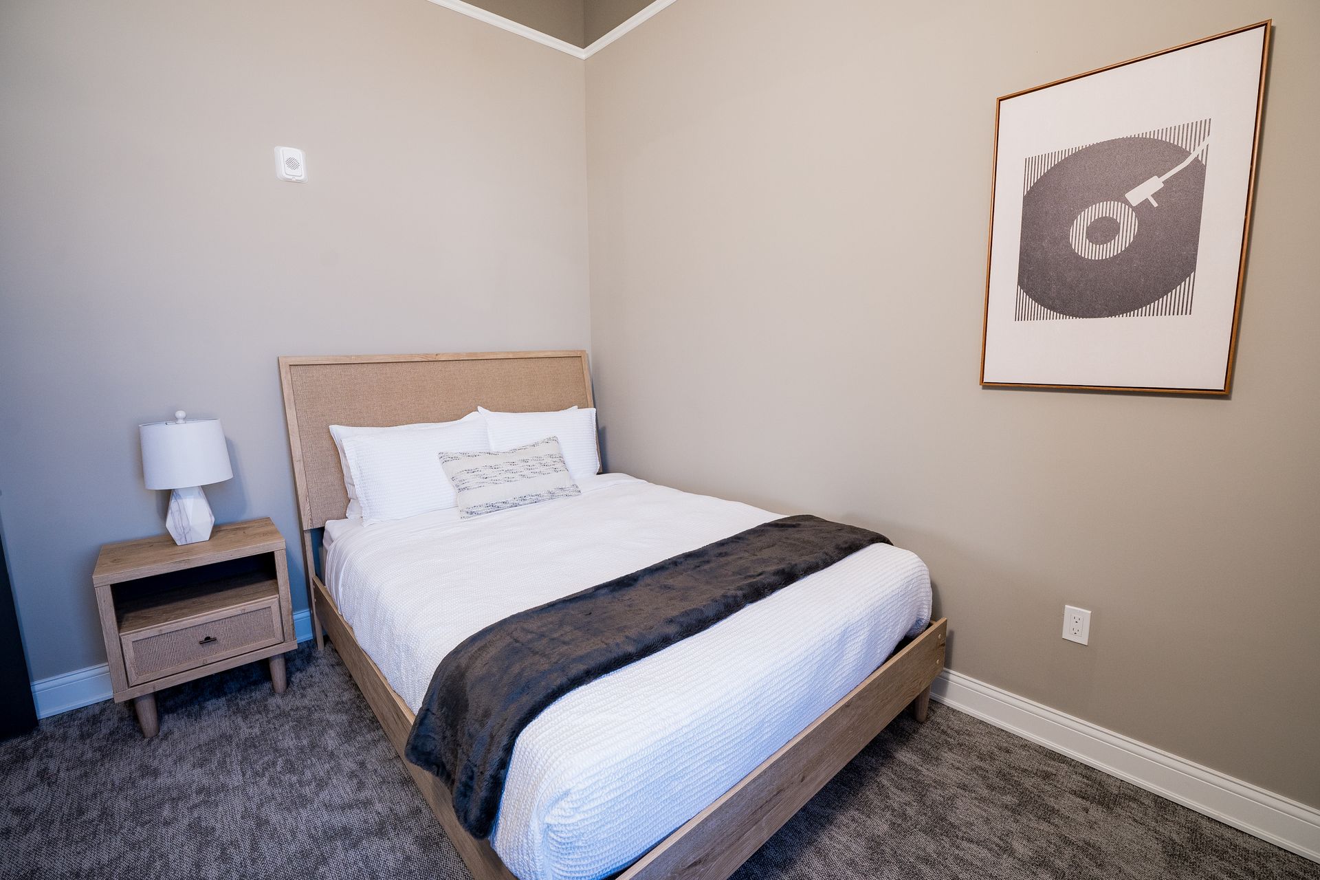 Small bedroom with a bed, nightstand, lamp, and framed wall art on beige walls.