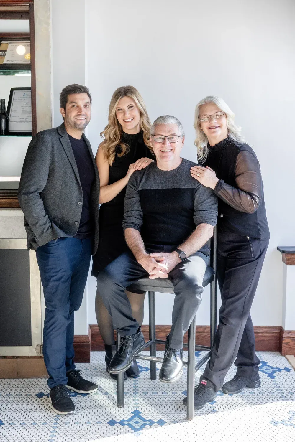 Four people posing indoors, with one seated on a stool and three standing behind.
