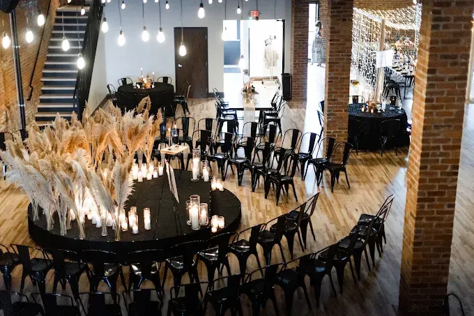 Elegant banquet hall with long black table, tall dried floral centerpieces, and rows of black chairs