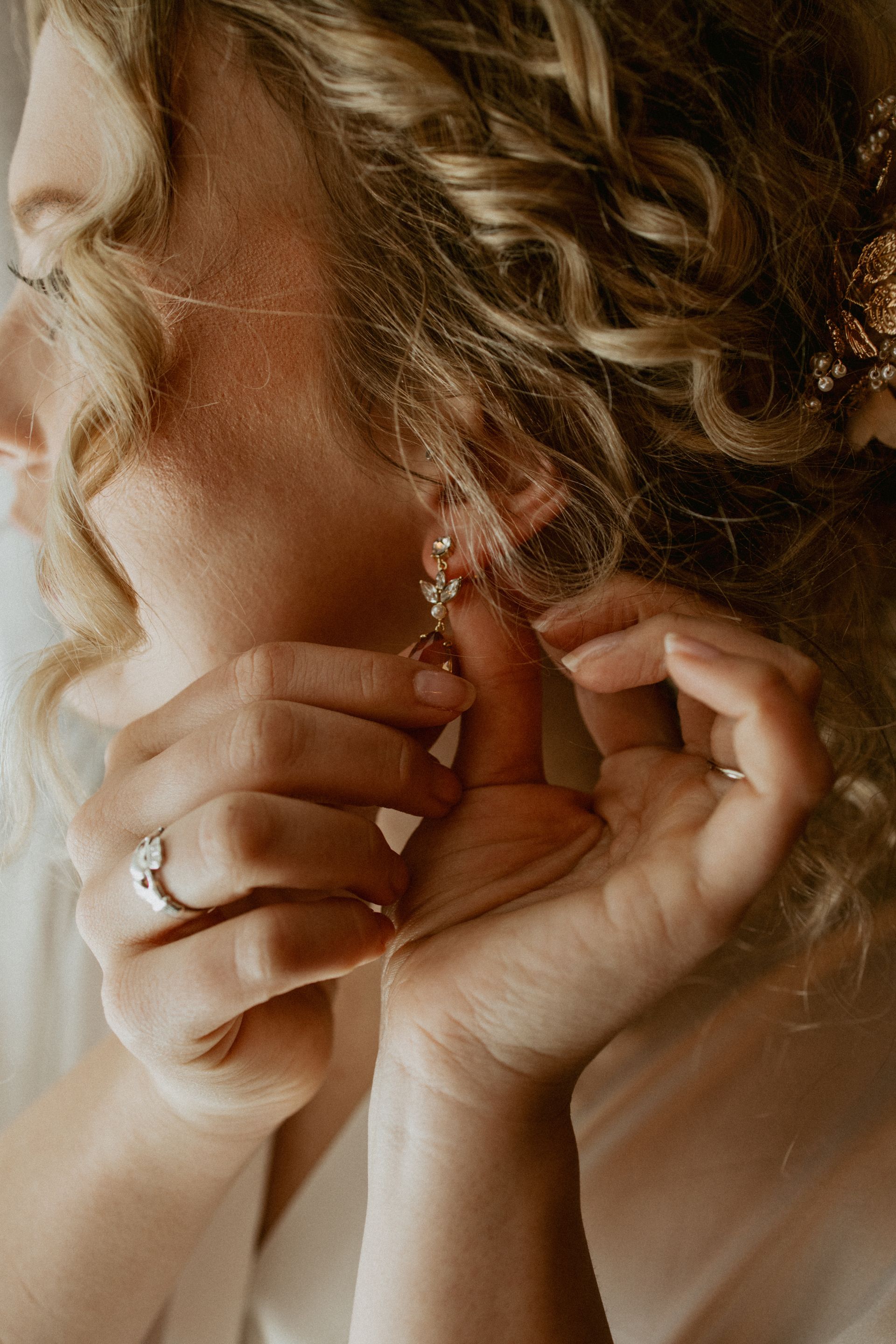 Hands fasten a dangling earring on a person with curly hair.
