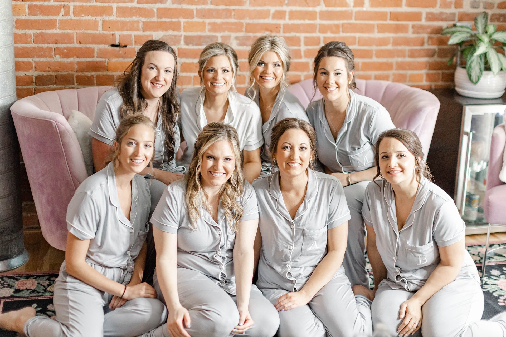 Group of six women in matching gray outfits sitting and standing in a cozy room with a brick wall.
